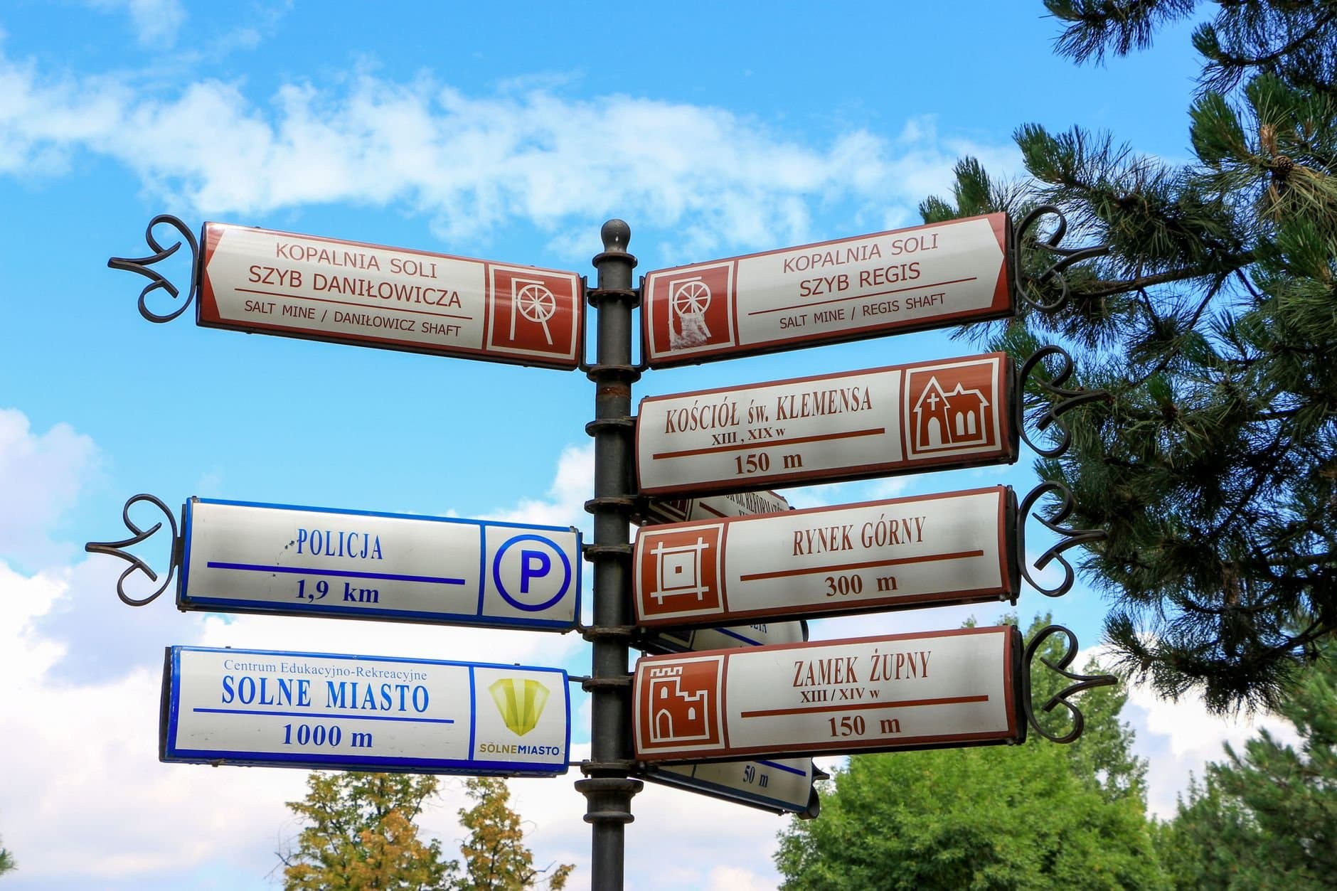 Signpost in Wieliczka, Poland, directing to salt mines and local attractions under a clear sky.