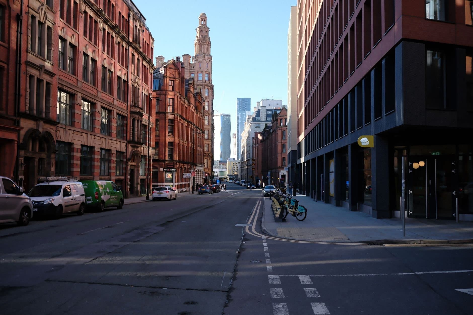 Urban streetscape in Manchester, showcasing modern and historic architecture under a clear blue sky.
