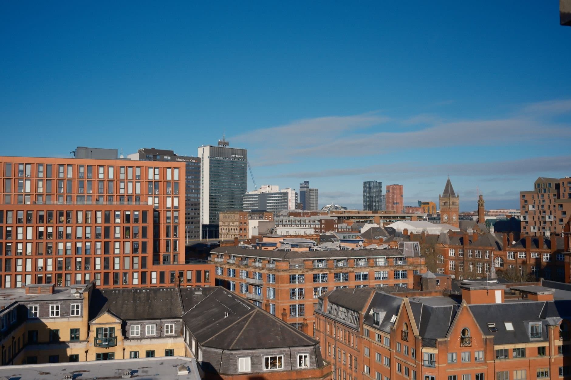 A vibrant cityscape of Manchester with modern and historical buildings under a clear blue sky.