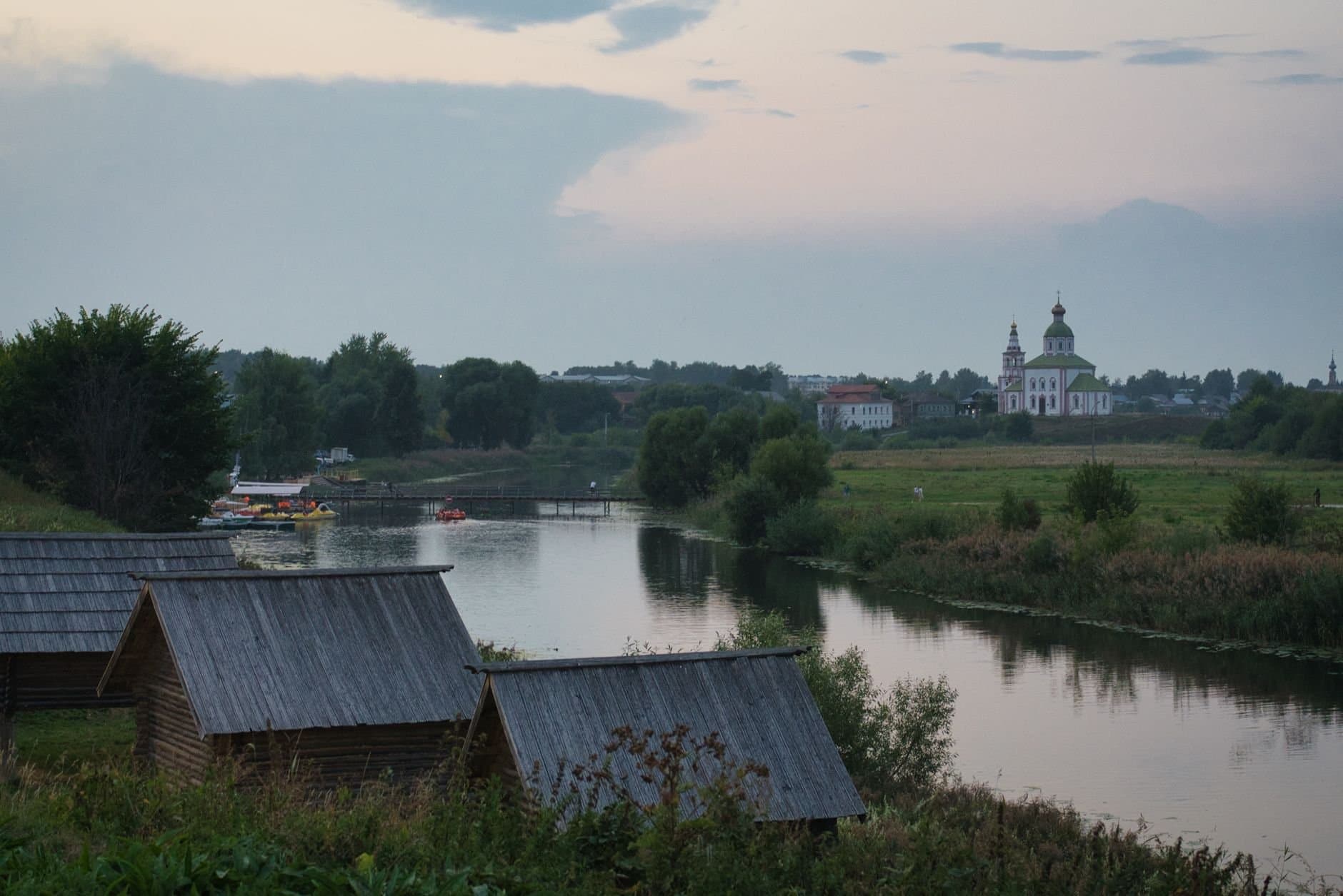 Scenic view of Suzdal's countryside with river and orthodox church at dusk.