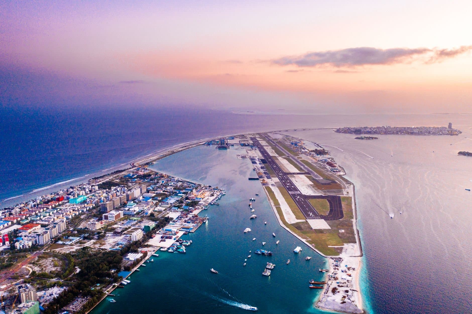 A breathtaking aerial view of a coastal city and airport at sunset with vibrant hues, capturing the blend of urban and natural beauty.