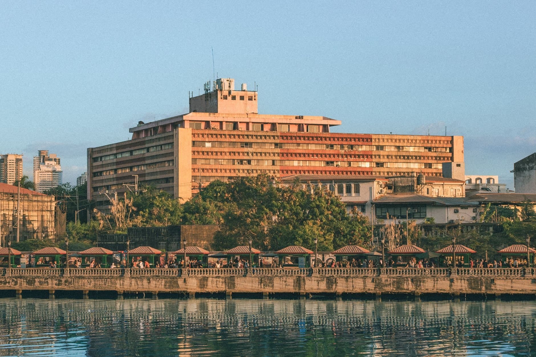 A scenic view of a historic riverside building in Manila during sunset, reflecting urban life.
