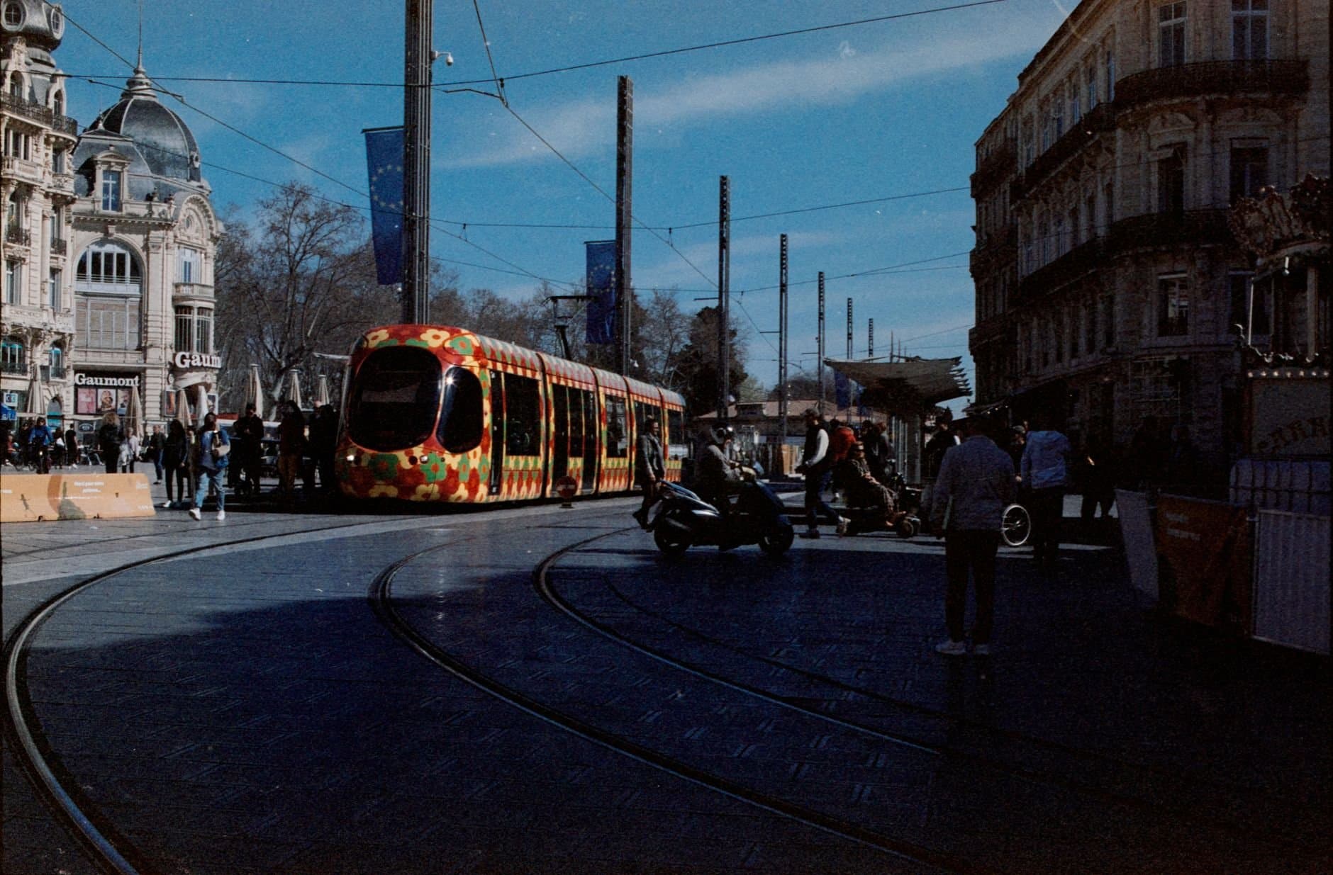 Colorful tram passing through a bustling street in Montpellier, France.