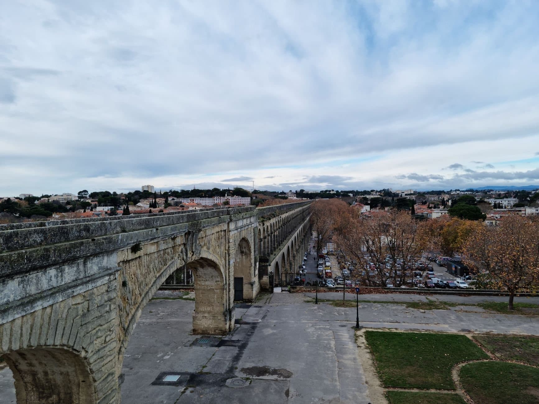 A scenic view of the historic Aqueduc Saint-Clément in Montpellier, showcasing its arches under a cloudy sky.