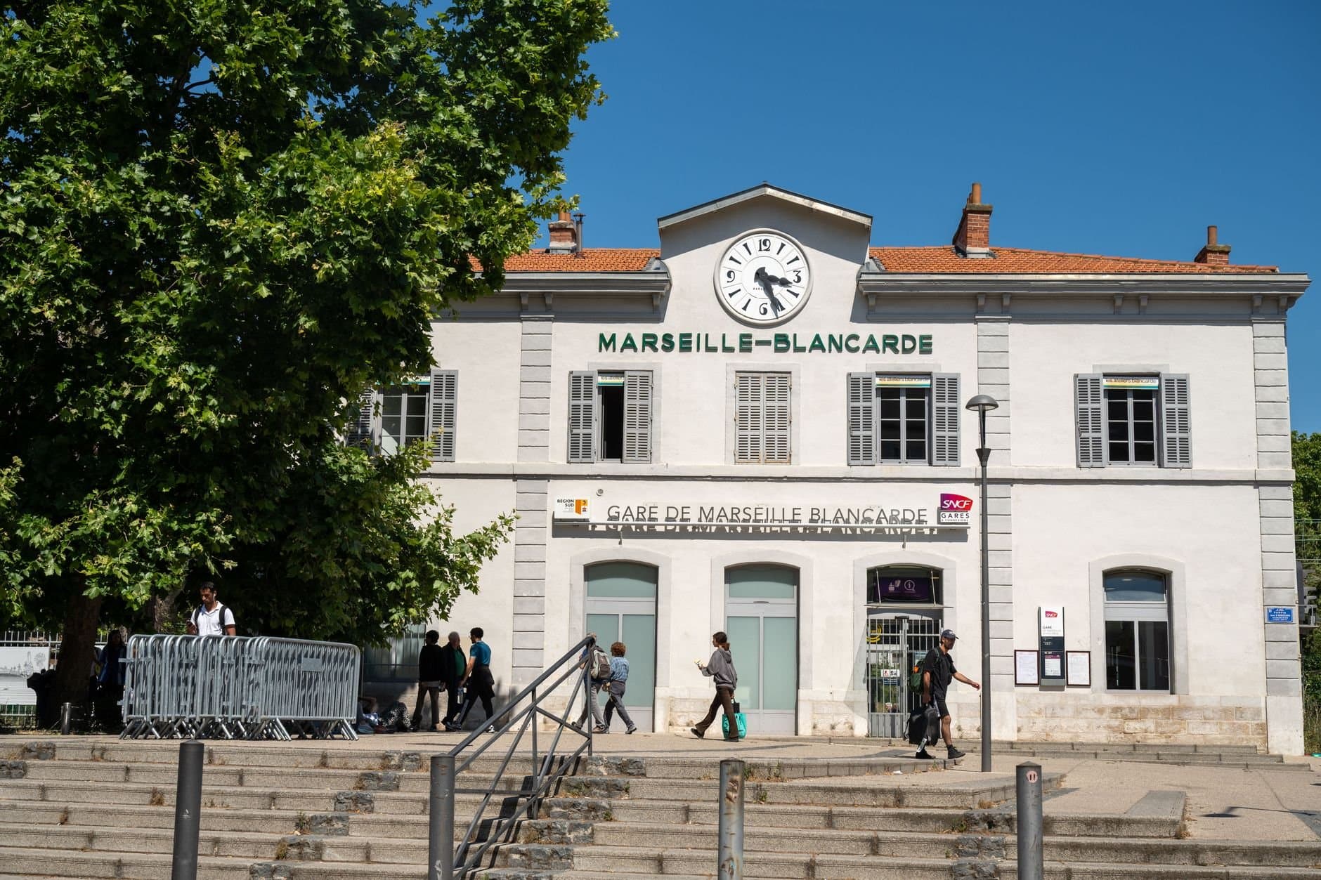 People walking in front of Gare de Marseille-Blancarde, a historic railway station in Marseille, France.