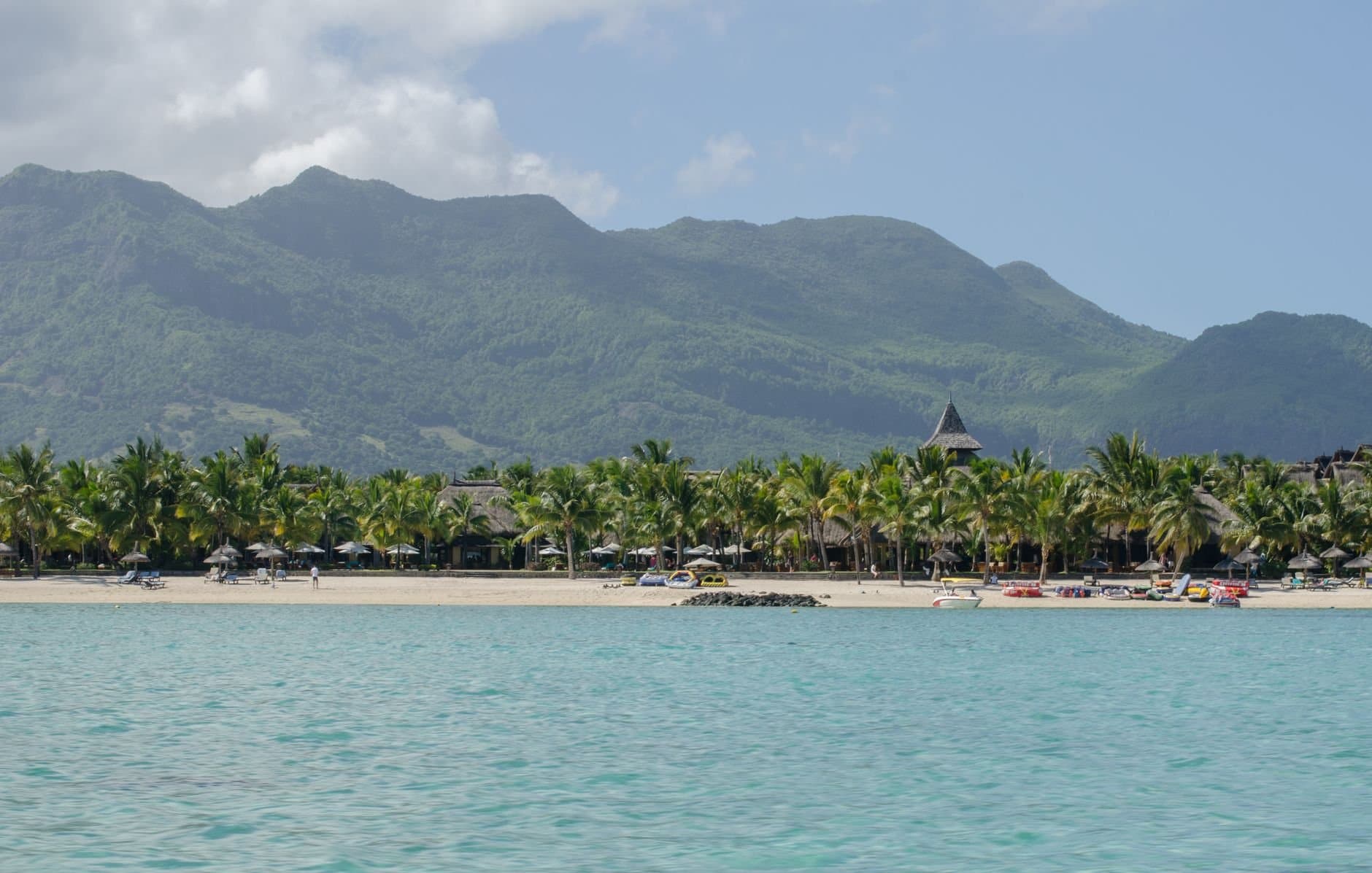 Peaceful tropical beach scene with palm trees, azure sea, and distant mountains.
