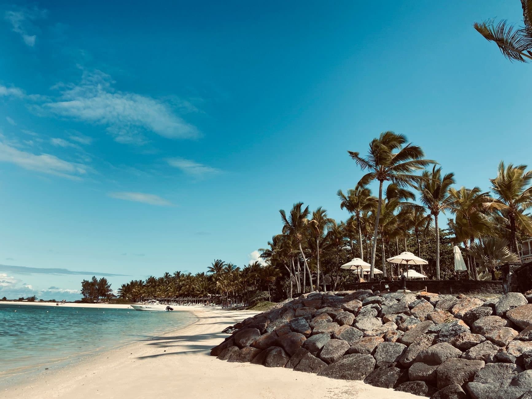 Serene sandy beach in Moka District, Mauritius, with clear blue skies and lush palm trees.