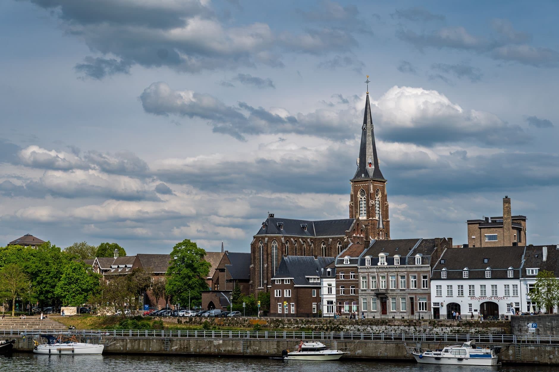 Scenic view of Maastricht with historic architecture and church by the river under cloudy skies.
