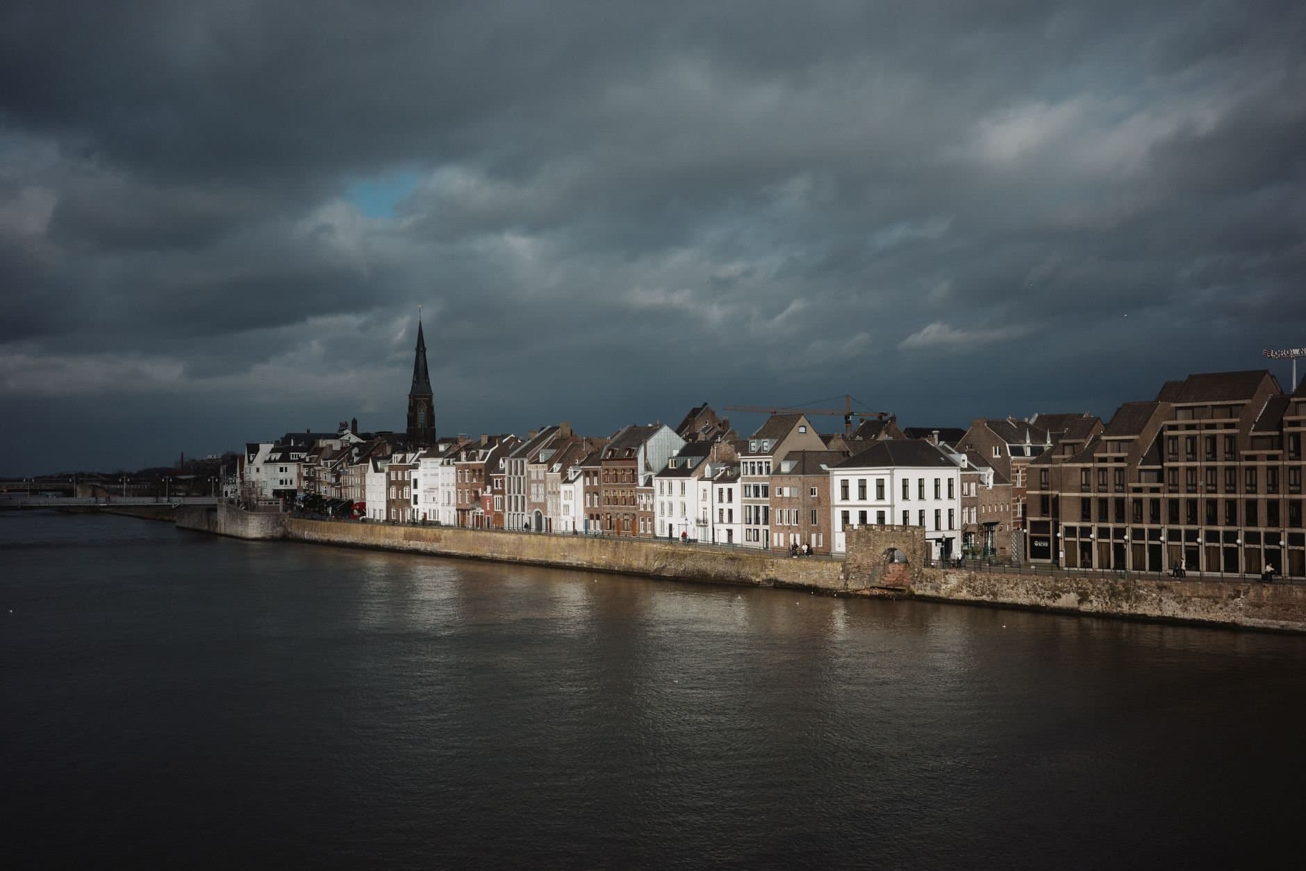 Picturesque view of Maastricht's riverside buildings under dramatic skies.