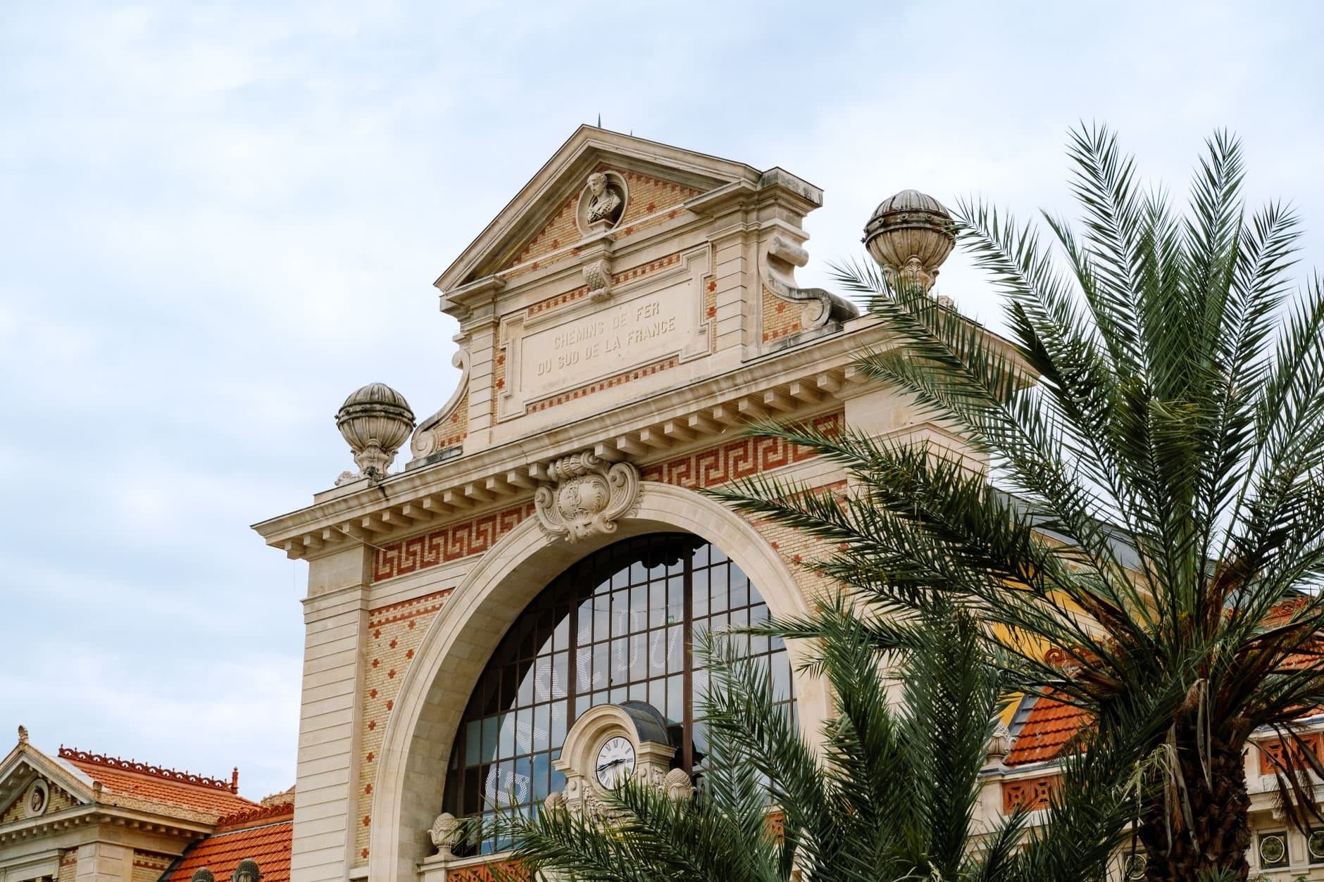 Classic French architecture with palm trees under a clear sky, highlighting intricate design and elegance.