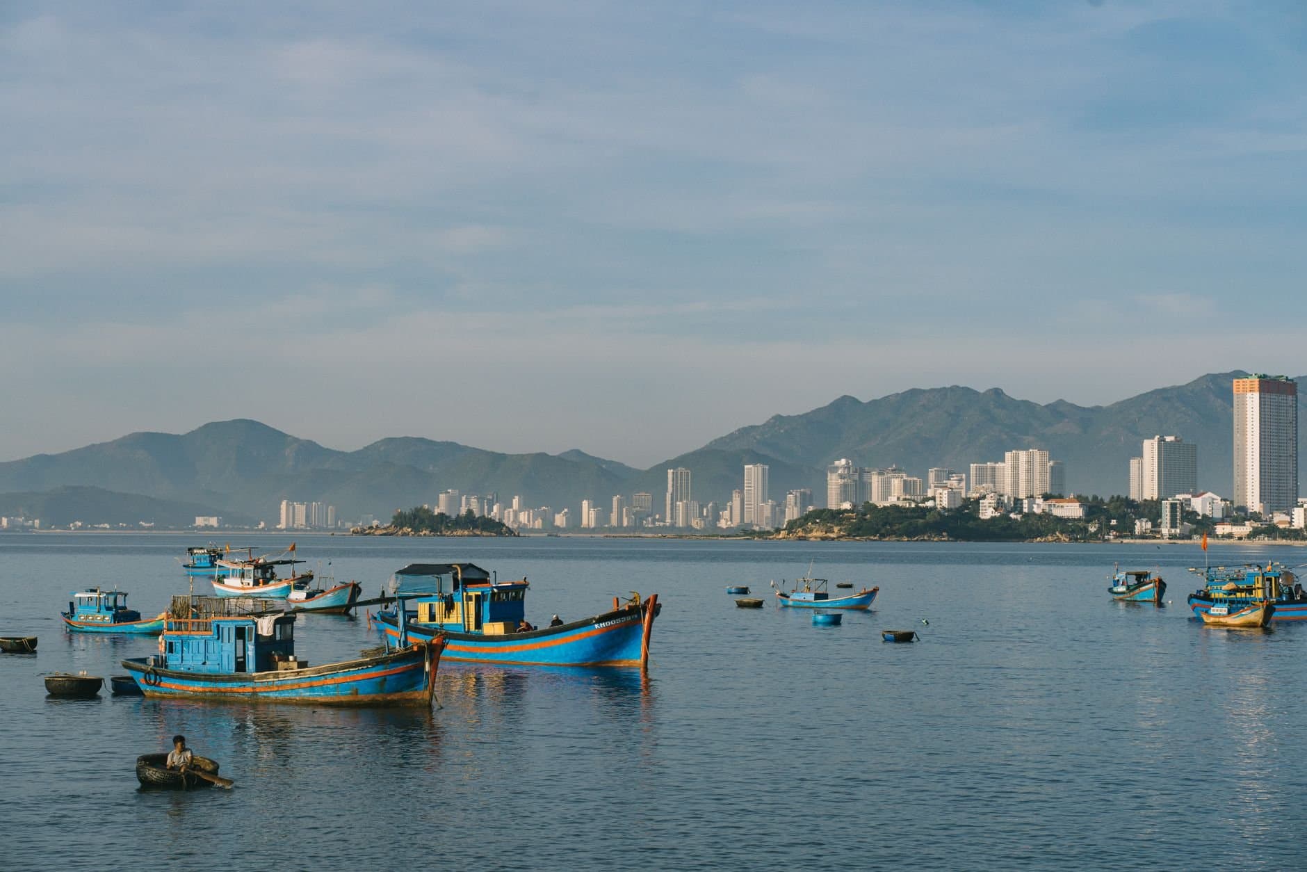 Vibrant fishing boats anchored with a city skyline and mountains in the background.