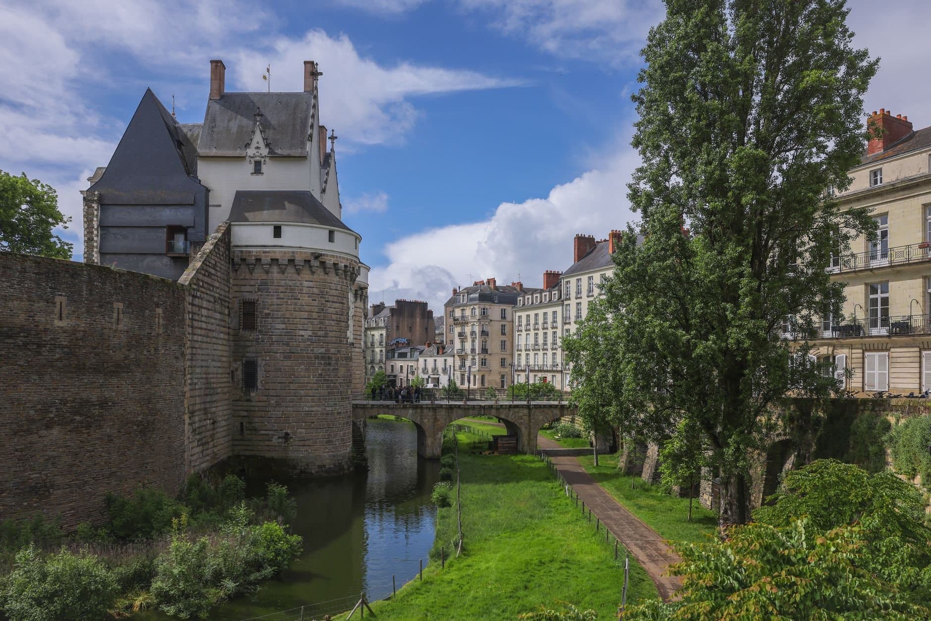 Scenic view of Château des Ducs de Bretagne with lush greenery and historic buildings in Nantes, France.