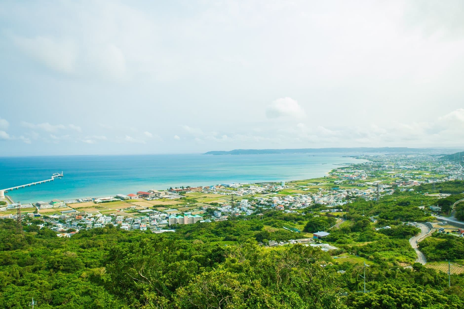 Calm turquoise water of ocean washing shore with small town and green tropical forest under cloudy sky