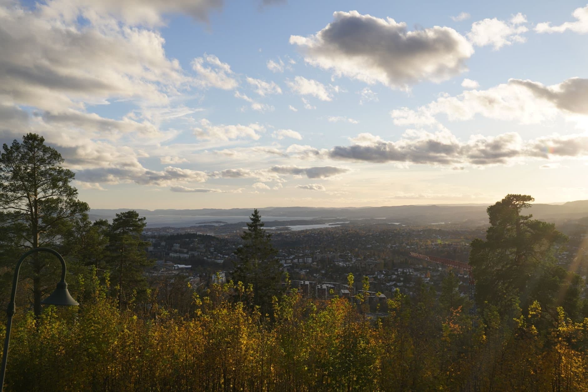 Scenic view of a city surrounded by trees and mountains under a sunset sky.