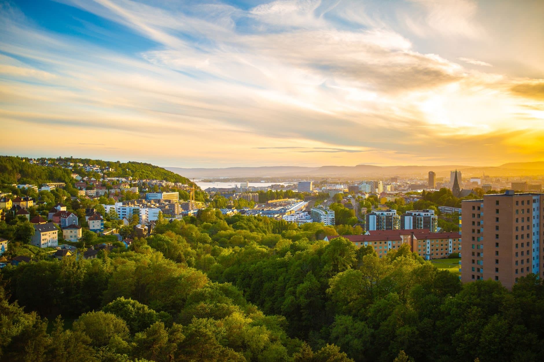 A breathtaking aerial view of Oslo, Norway, featuring lush greenery and a vibrant sunset sky.