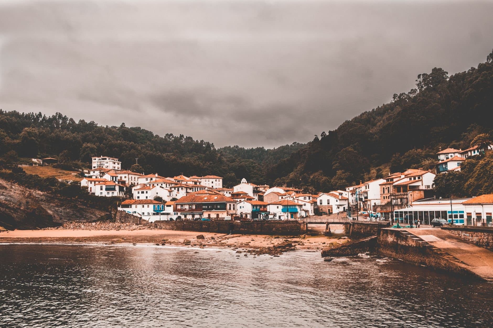 Charming coastal town of Candás, Spain under overcast skies with traditional houses along the waterfront.
