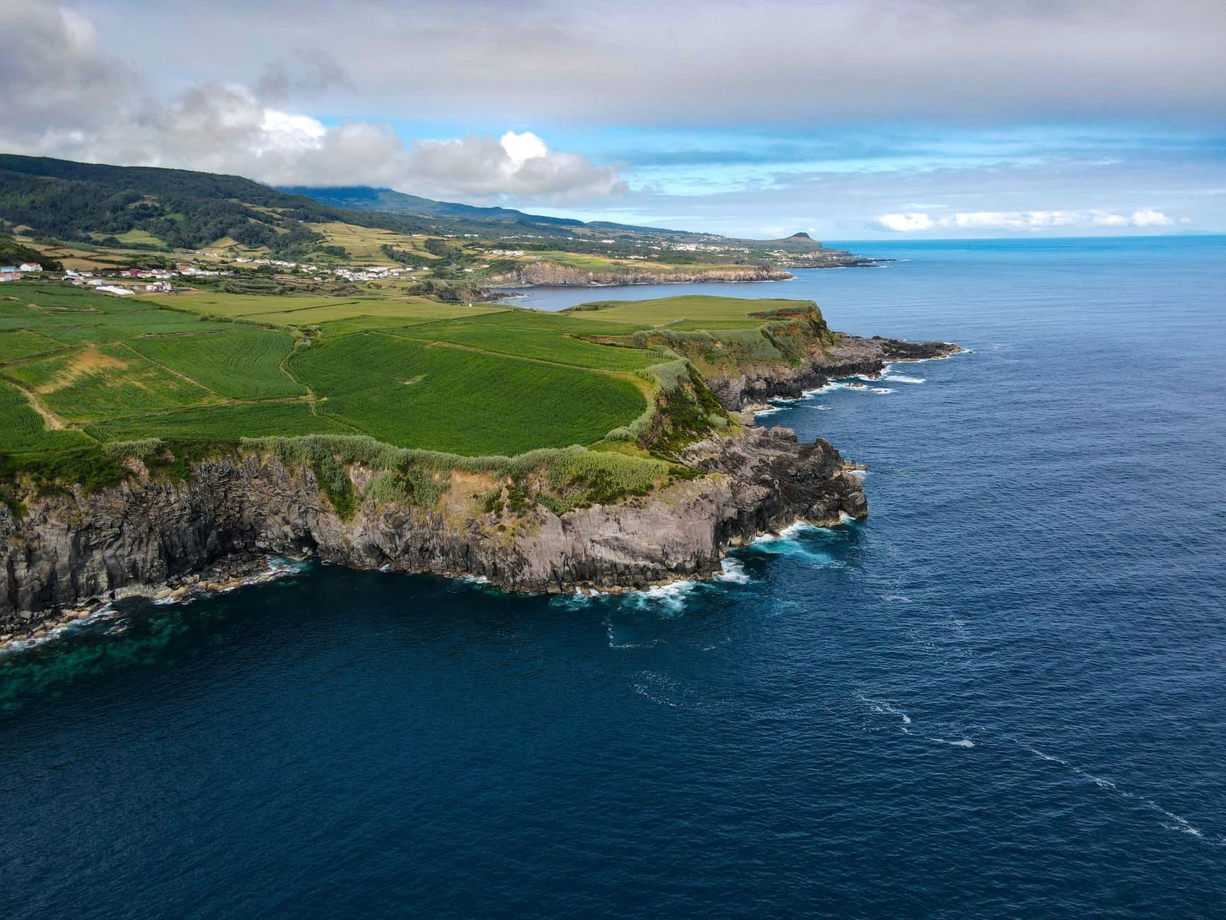 Stunning aerial view of coastal cliffs and ocean with lush greenery and distant landscape.