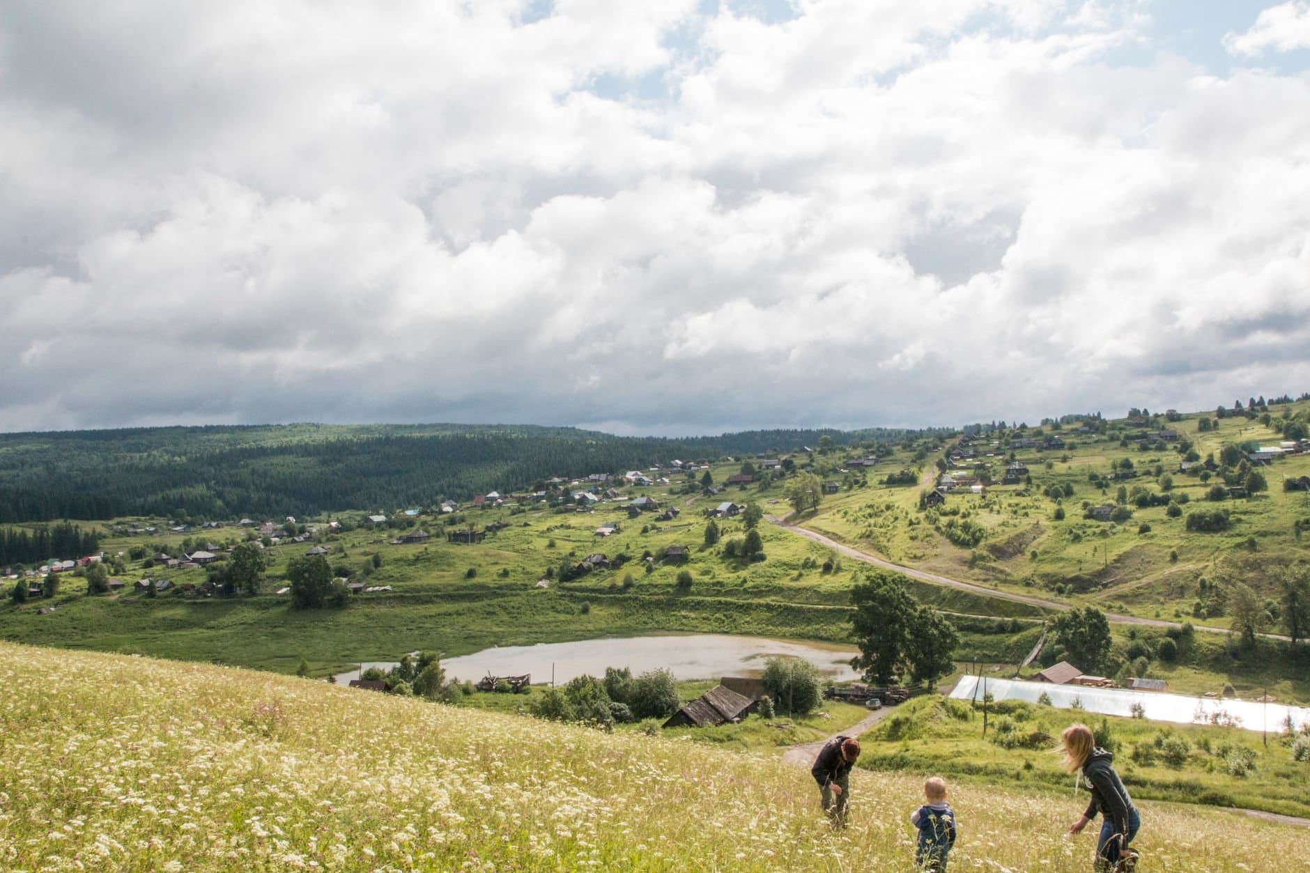 Russian countryside scene with rolling hills, clouds, and a village.