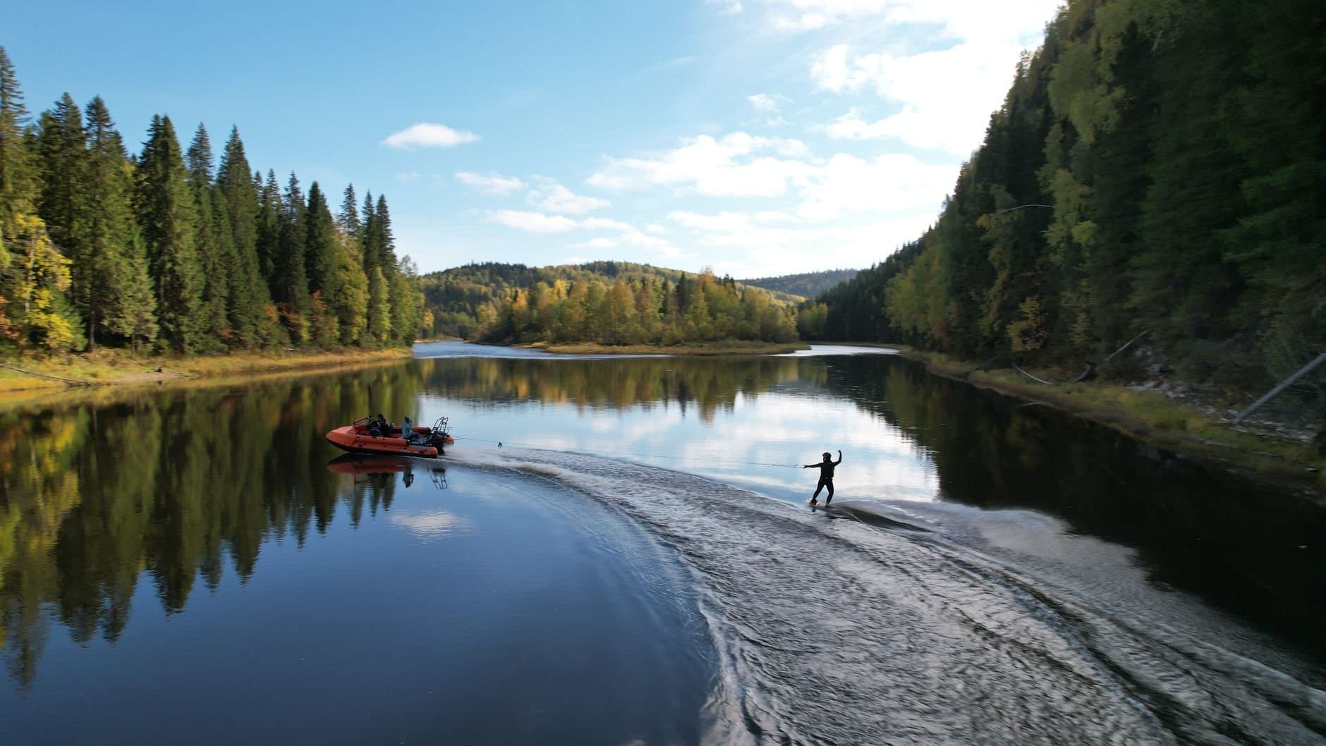 A wakeboarder enjoys a thrilling ride on a serene river surrounded by lush forests in the Ural Mountains, Russia.
