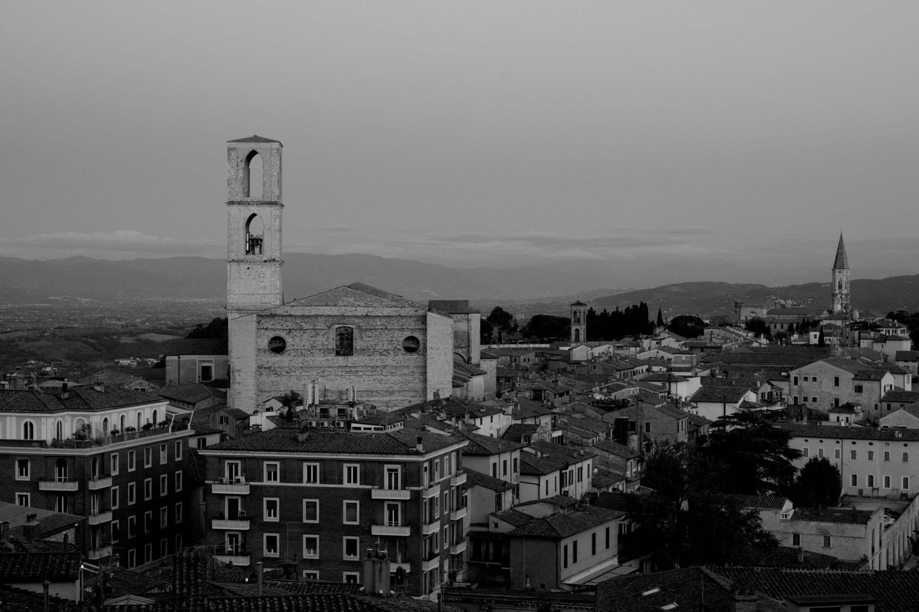 Aerial black and white view of a historic Italian cityscape featuring medieval architecture and bell towers.