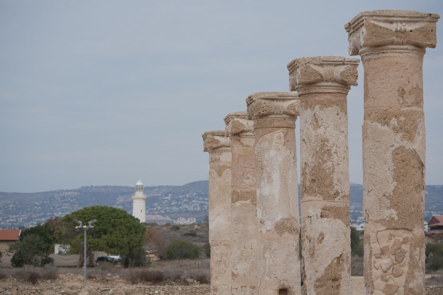 Ancient stone columns with a lighthouse in the background under a clear sky.