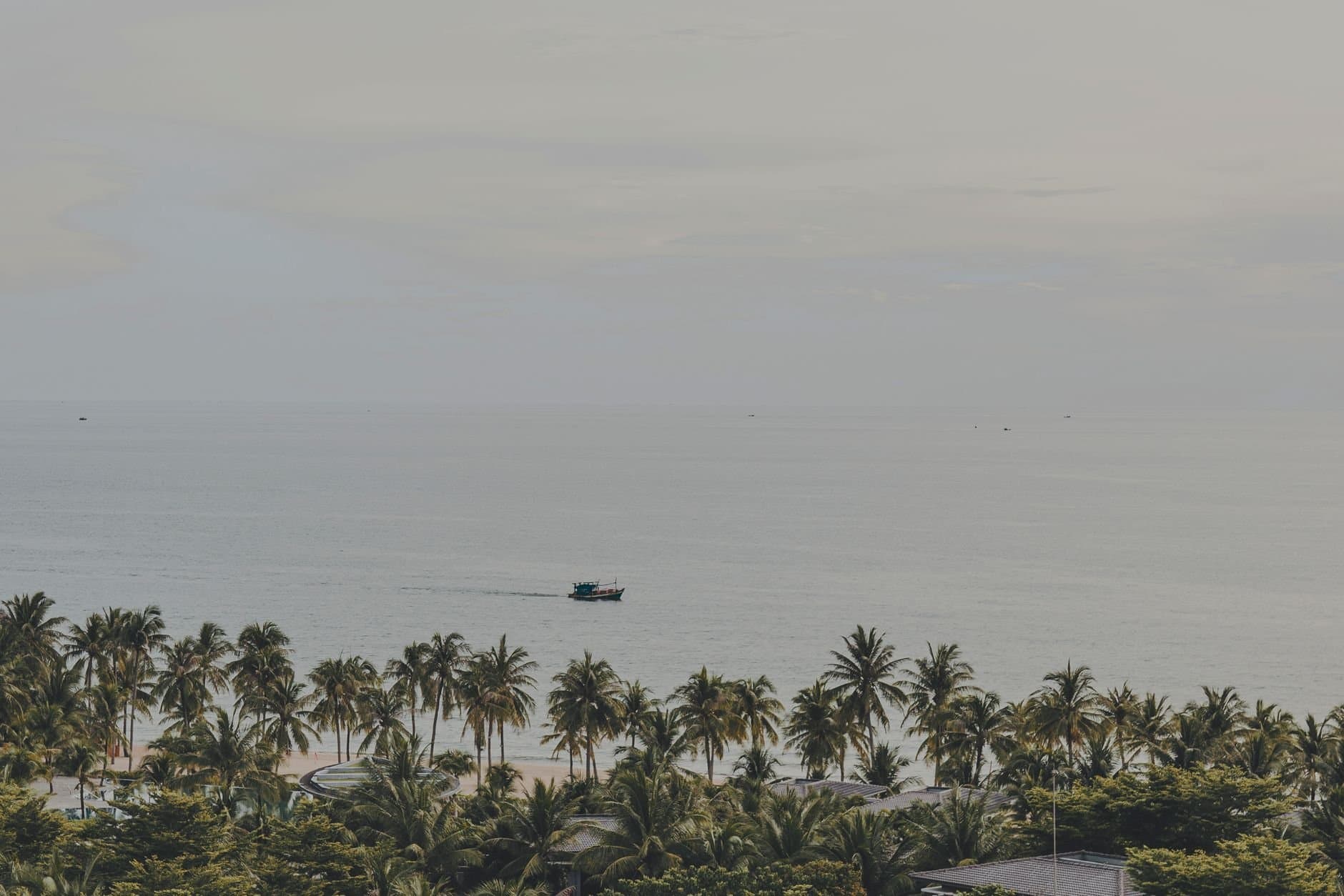 Serene panorama of palm-lined Phu Quoc beach with a distant boat on the calm sea.