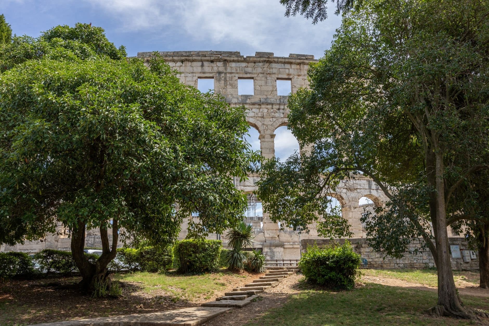 A serene view of the ancient Roman amphitheater in Pula, Croatia, framed by lush green trees.