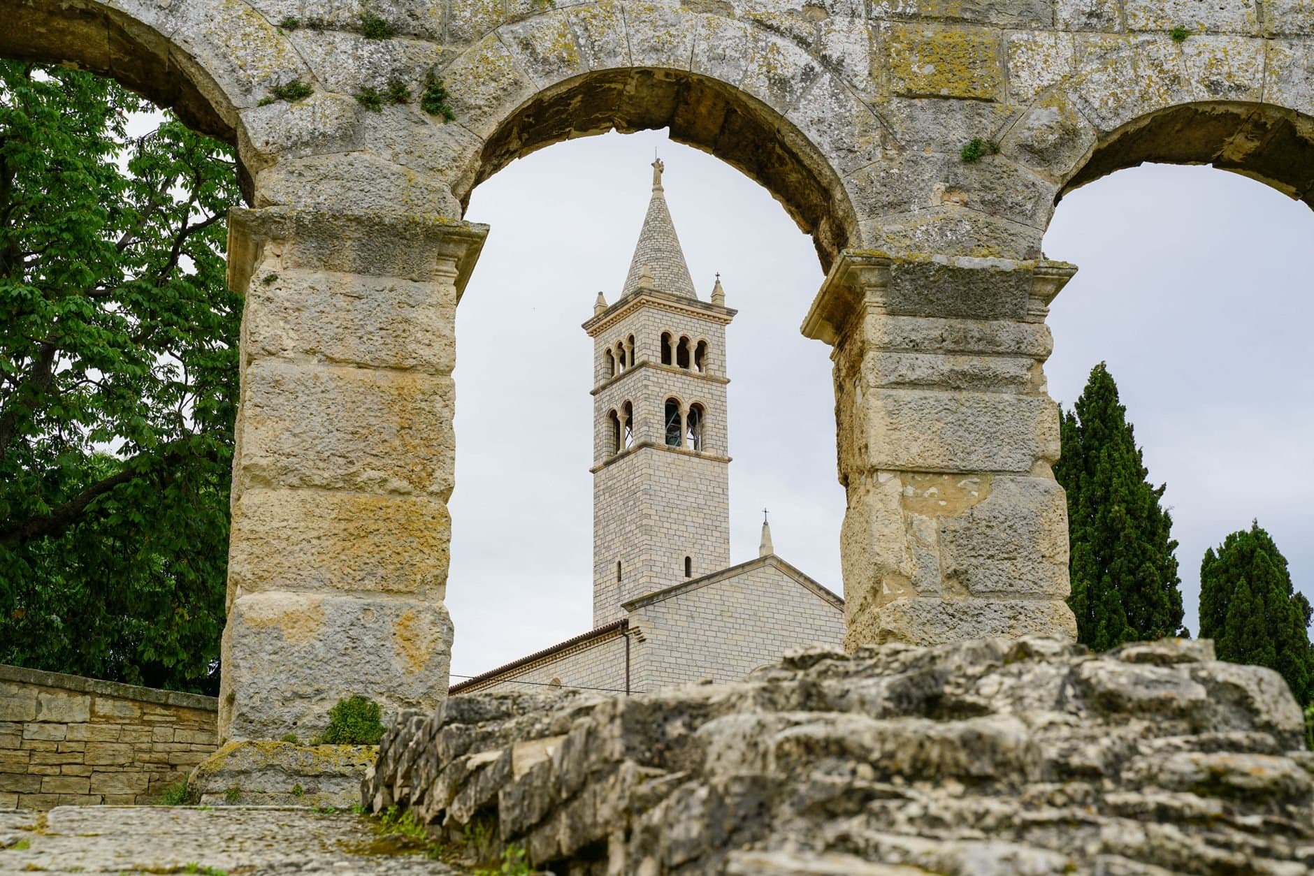 Ancient stone arches framing a historic church tower in Pula, Croatia.