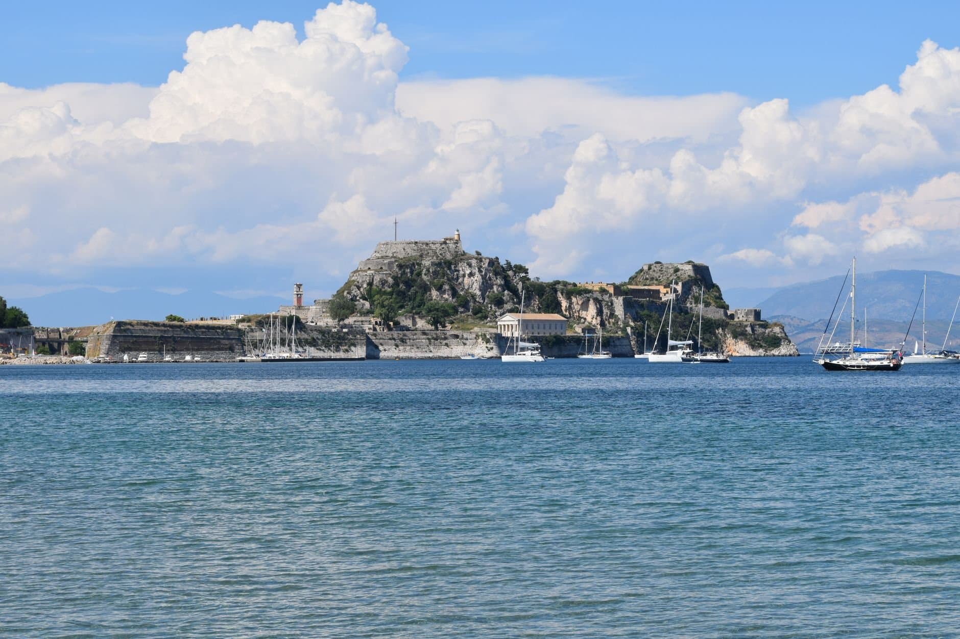 Scenic view of Corfu's old fortress and sailboats under a blue sky.