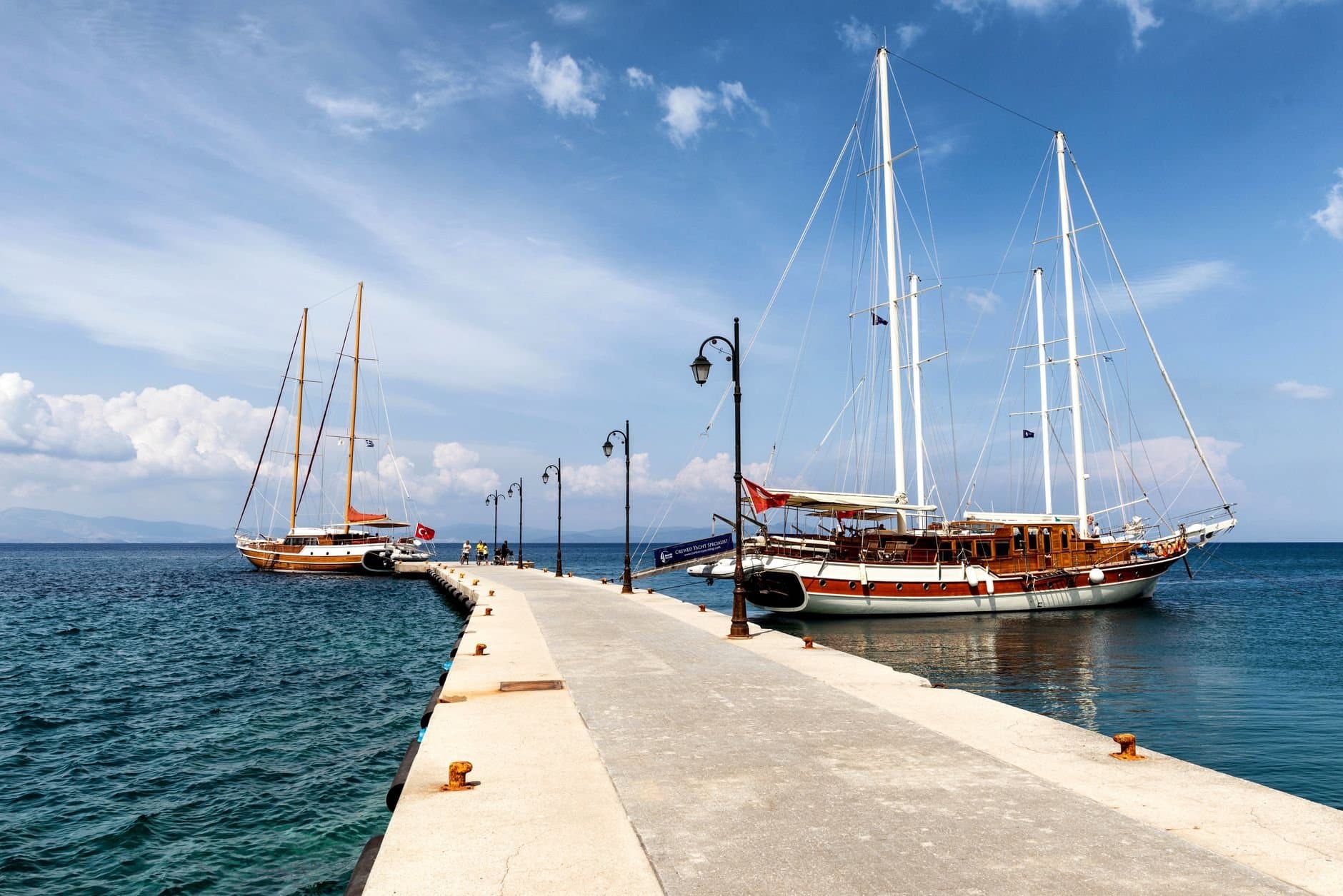 Sailboats moored at a scenic pier in Kos, Greece under a bright summer sky.