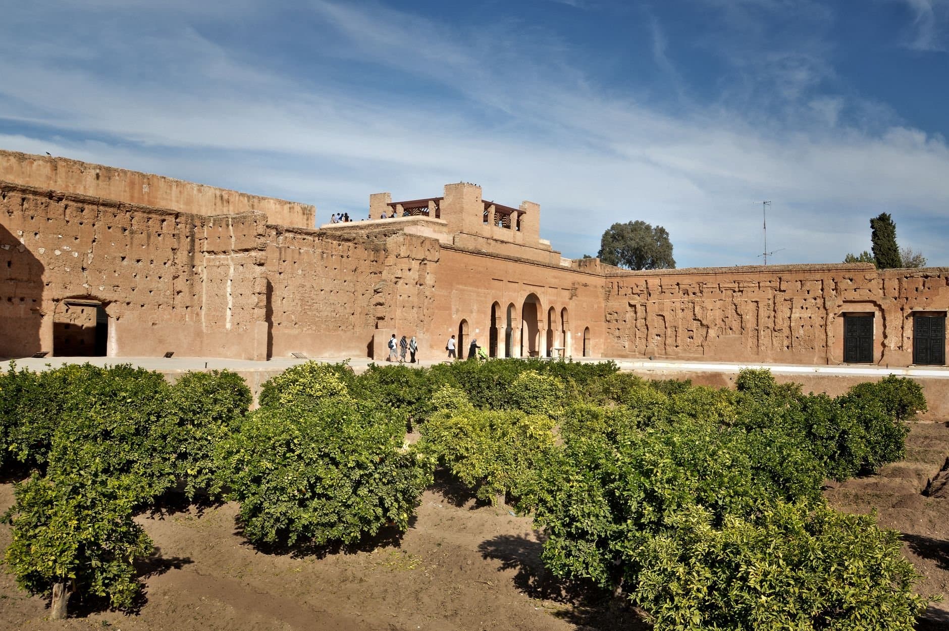 View of historic red walls and lush gardens under a blue sky in Marrakesh, Morocco.