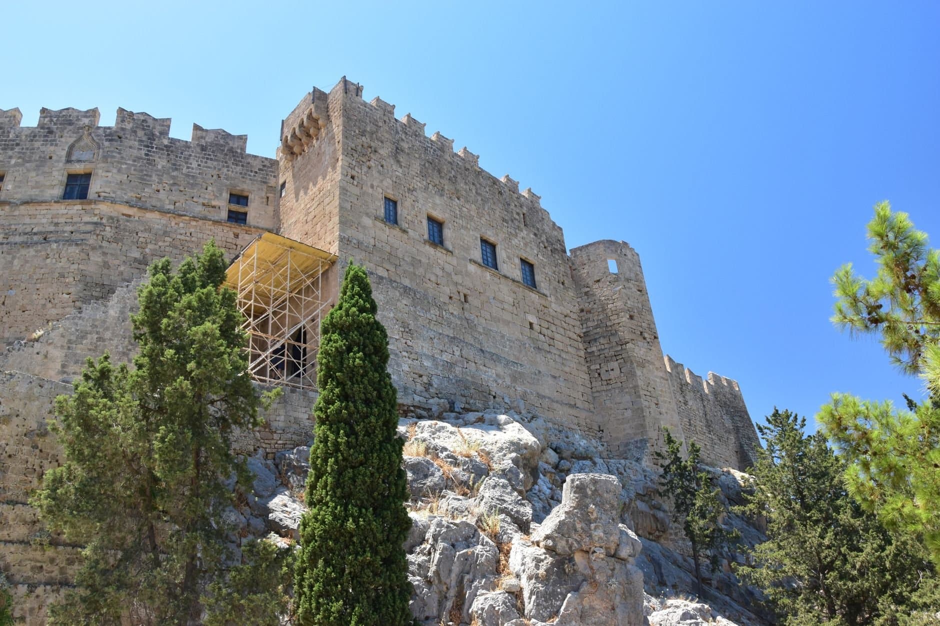 A majestic medieval stone fortress set against a vivid blue sky, surrounded by lush trees.