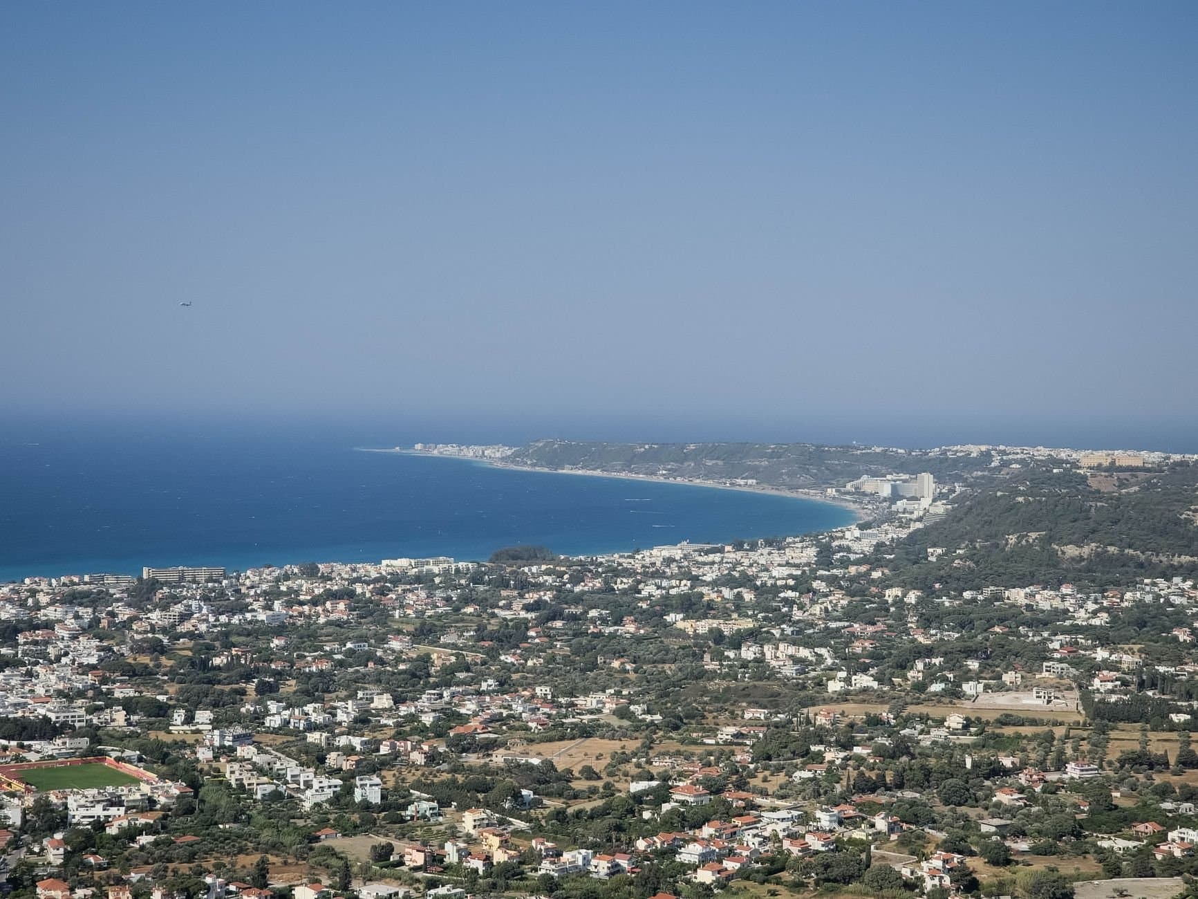 Stunning aerial view of a coastal cityscape and azure sea in Greece on a sunny day.