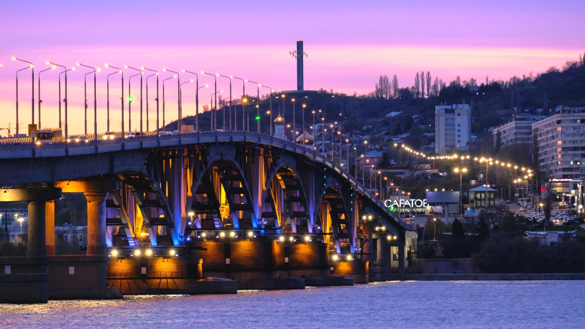 Stunning twilight view of a bridge in Saratov, Russia, with vibrant street lights and city skyline.