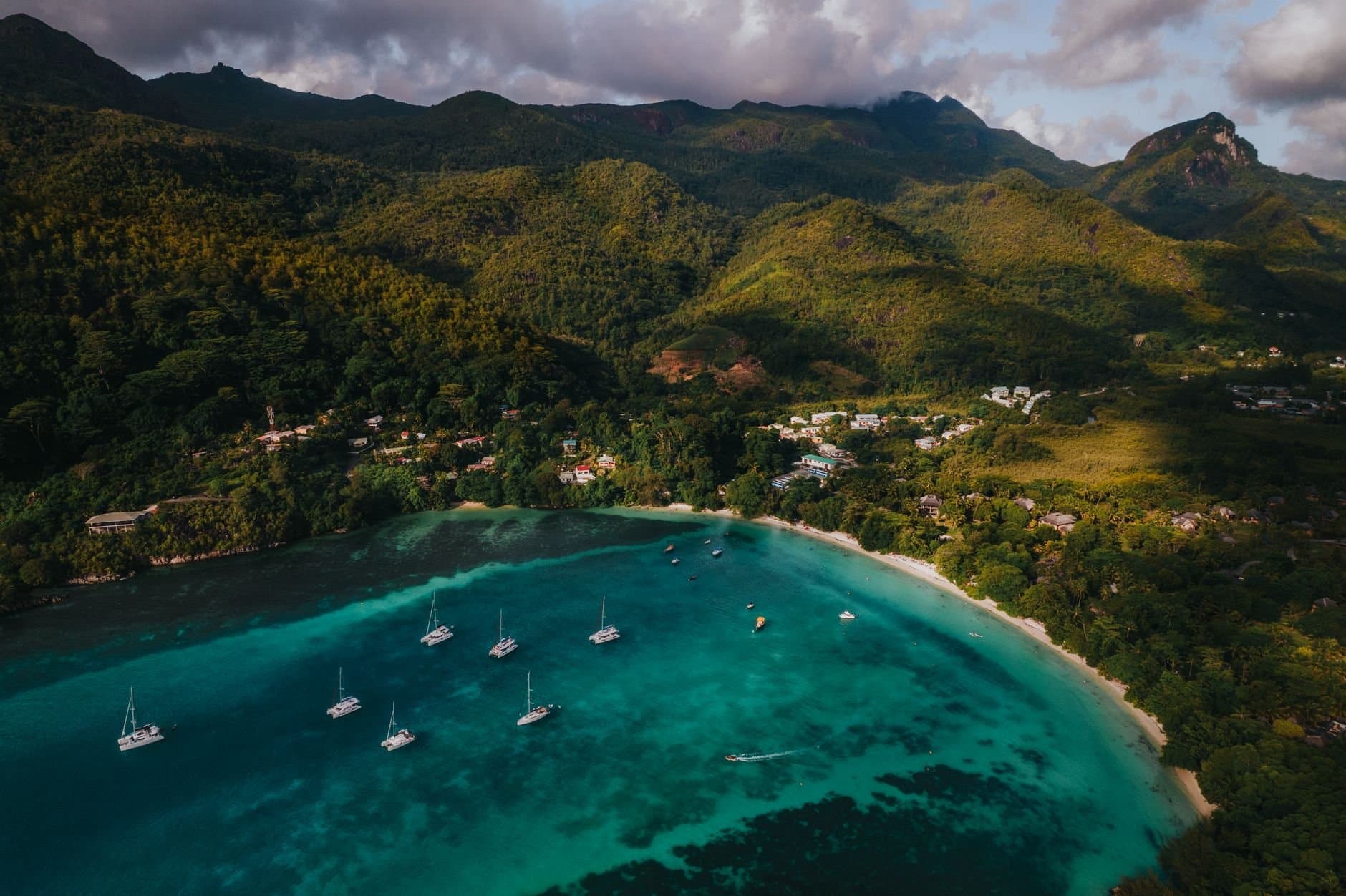 Stunning aerial view of a bay in Seychelles with anchored yachts, lush greenery, and turquoise waters.