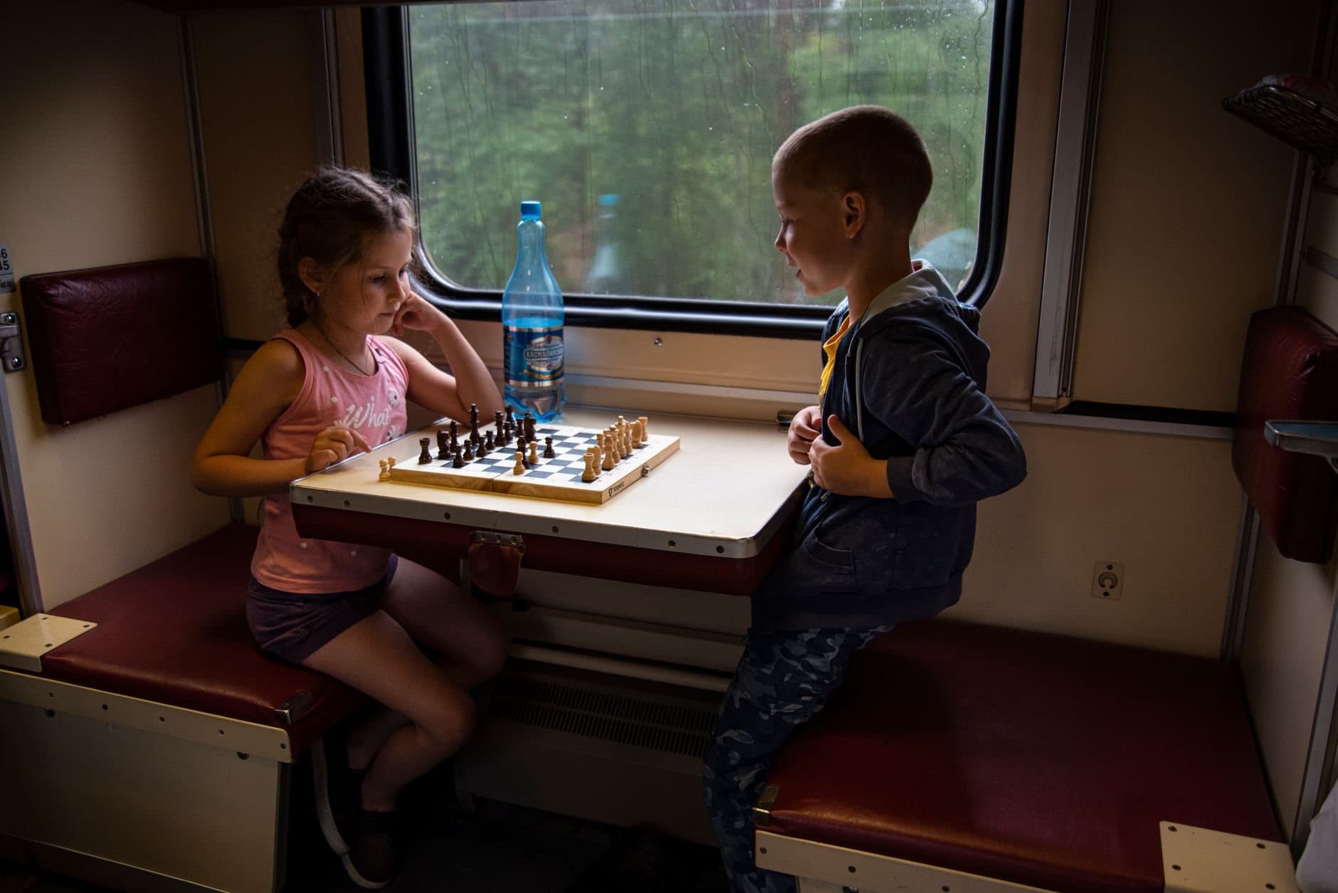Two kids playing chess onboard a train in Russia, capturing childhood and travel themes.