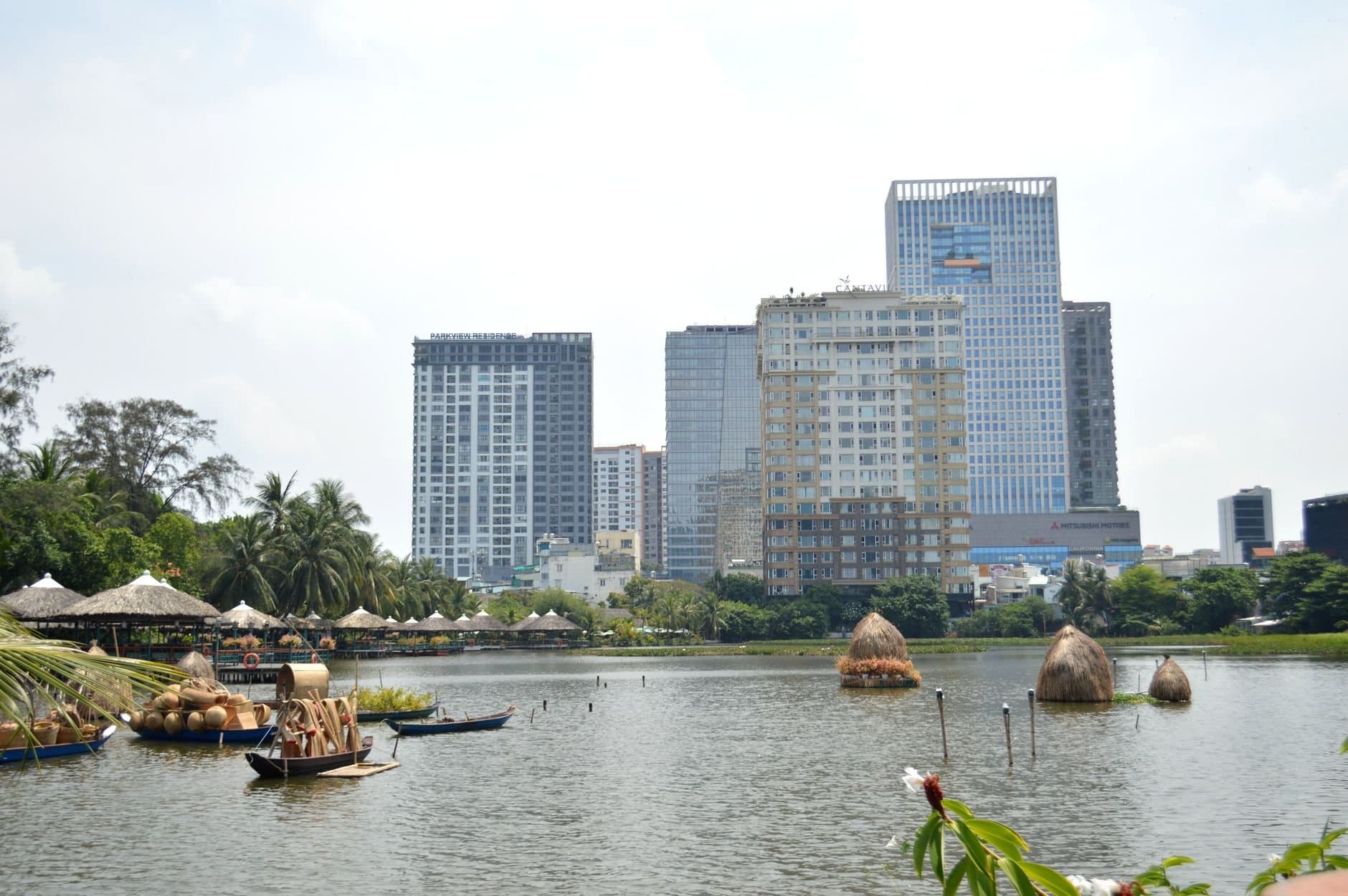 A scenic cityscape featuring skyscrapers along a river with boats and greenery.