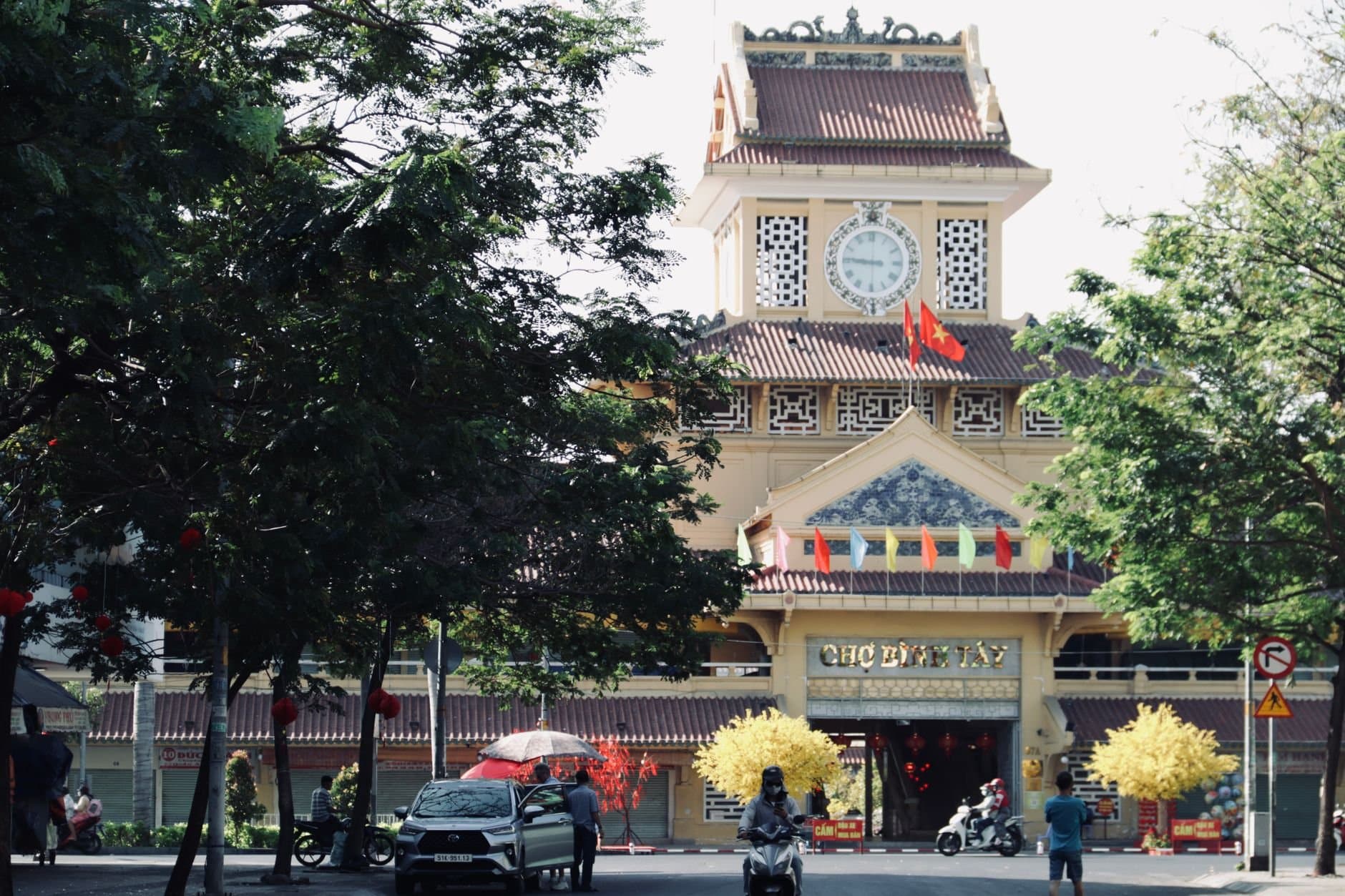 Scenic view of the iconic Binh Tay Market entrance with surrounding trees and vibrant flags in Ho Chi Minh City, Vietnam.