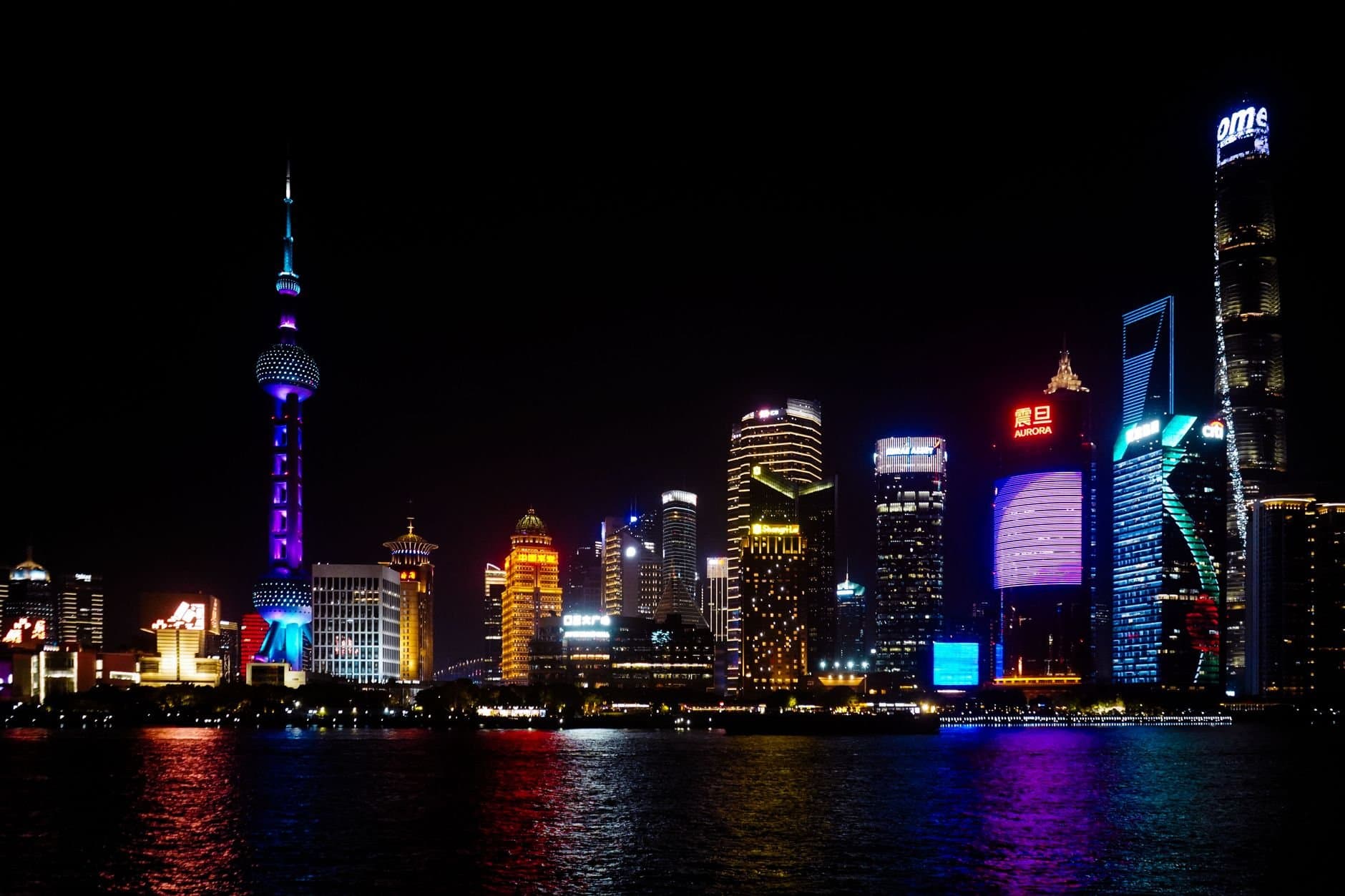 Vibrant Shanghai skyline at night featuring iconic skyscrapers and colorful lighting reflections on water.