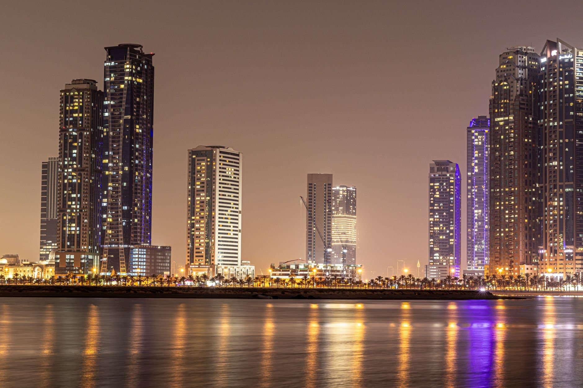Stunning night view of Sharjah's modern skyline reflected in calm water.