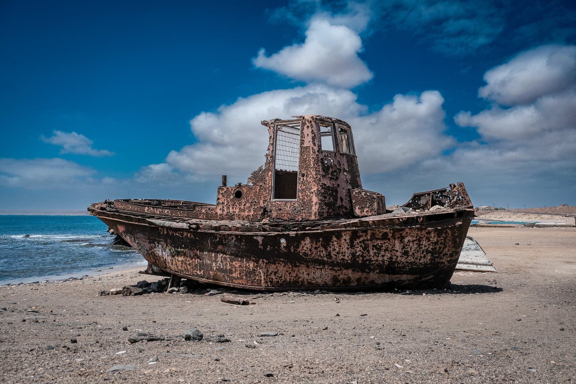 An abandoned rusty boat on the sandy shores of Pedra Lume, Sal Island, under a vivid blue sky.
