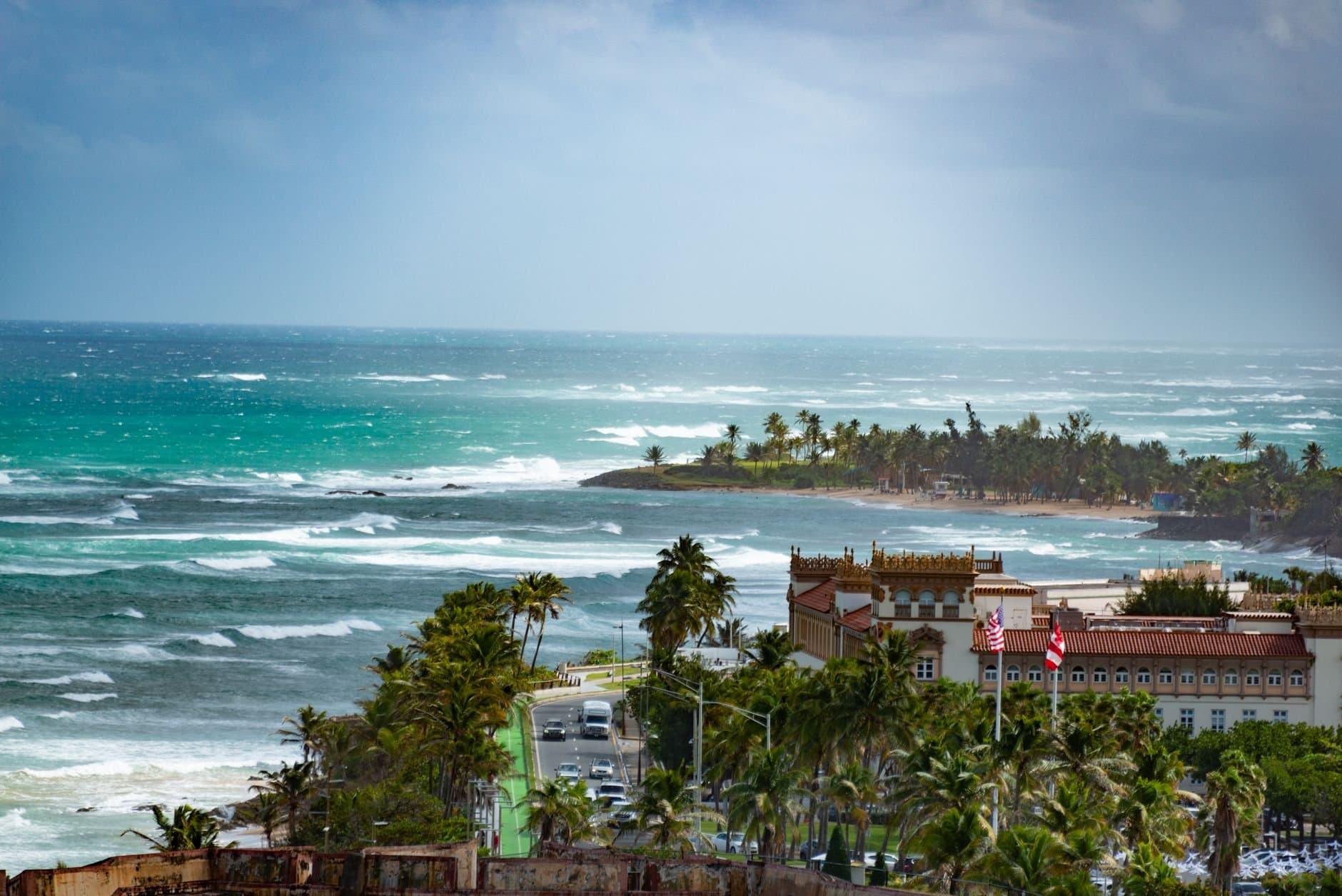 A breathtaking aerial view of a tropical coastline with waves crashing against the shore and lush palm trees.