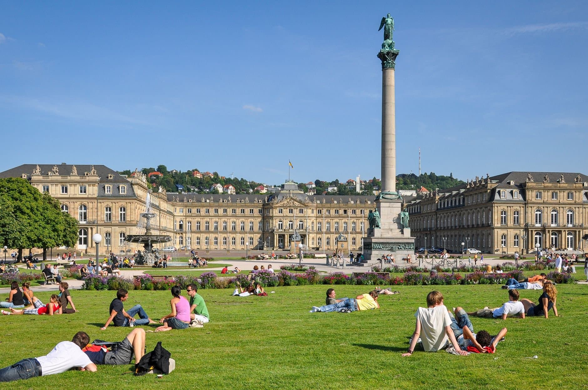 People relaxing on the grass at Schlossplatz, Stuttgart, under a sunny sky with Neues Schloss in the background.
