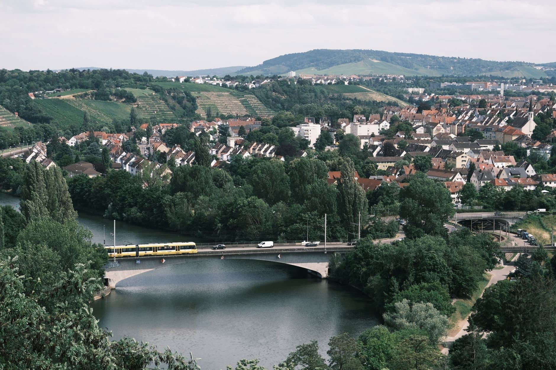 Aerial view of Stuttgart with vineyard hills, the River Neckar, and a bridge crossing the river, showcasing urban and natural beauty.