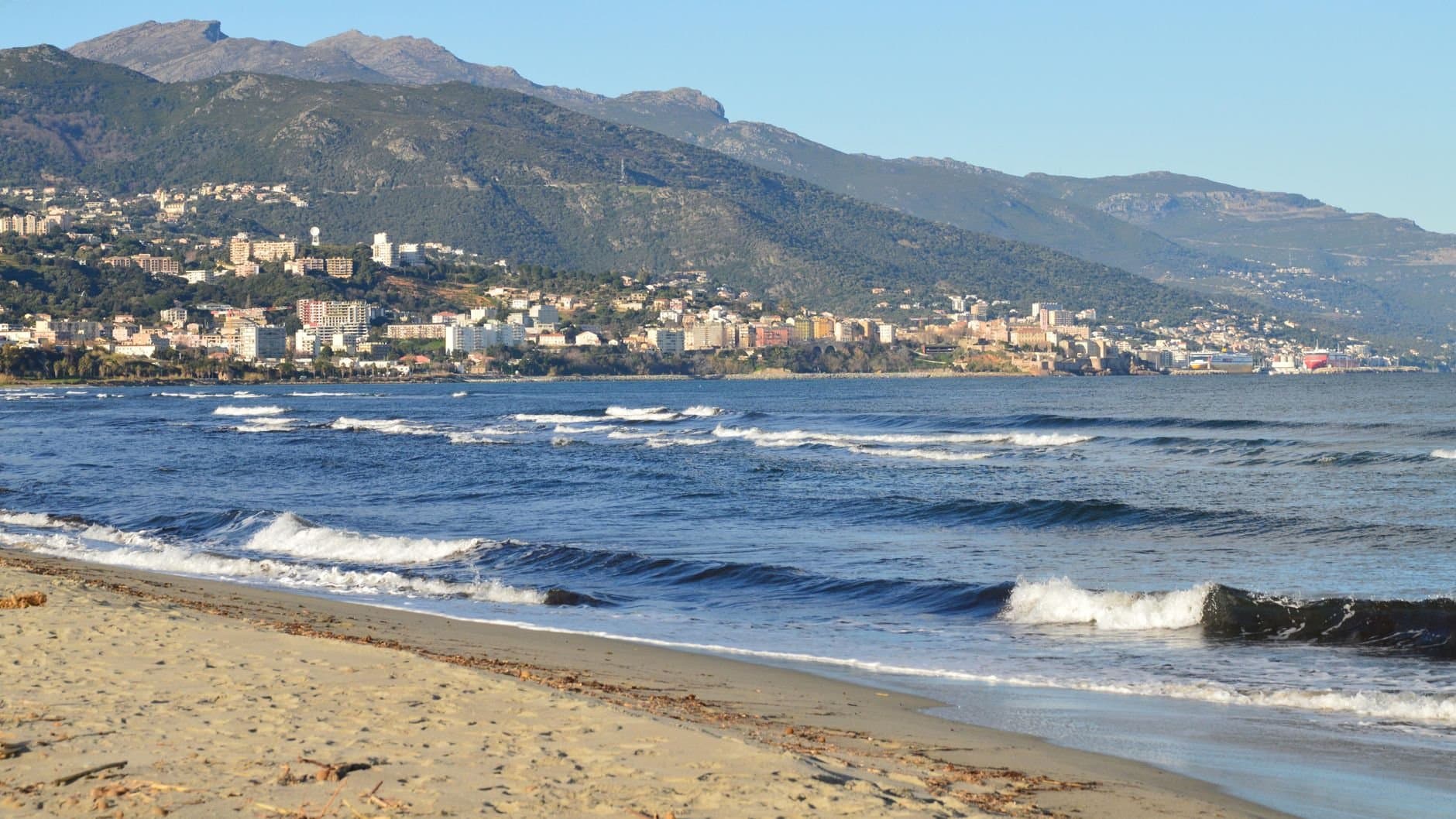 Beautiful coastal view of Bastia, Corse, France with waves, beach, and mountains.