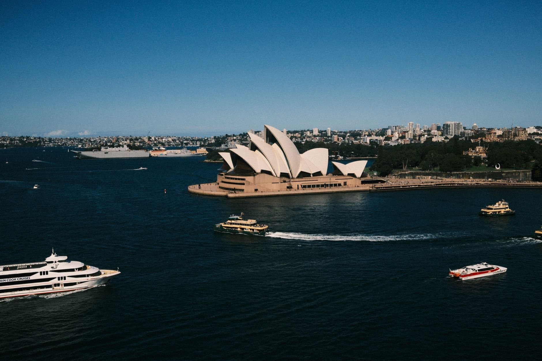 A breathtaking aerial view capturing the iconic Sydney Opera House surrounded by ferry boats on a sunny day.