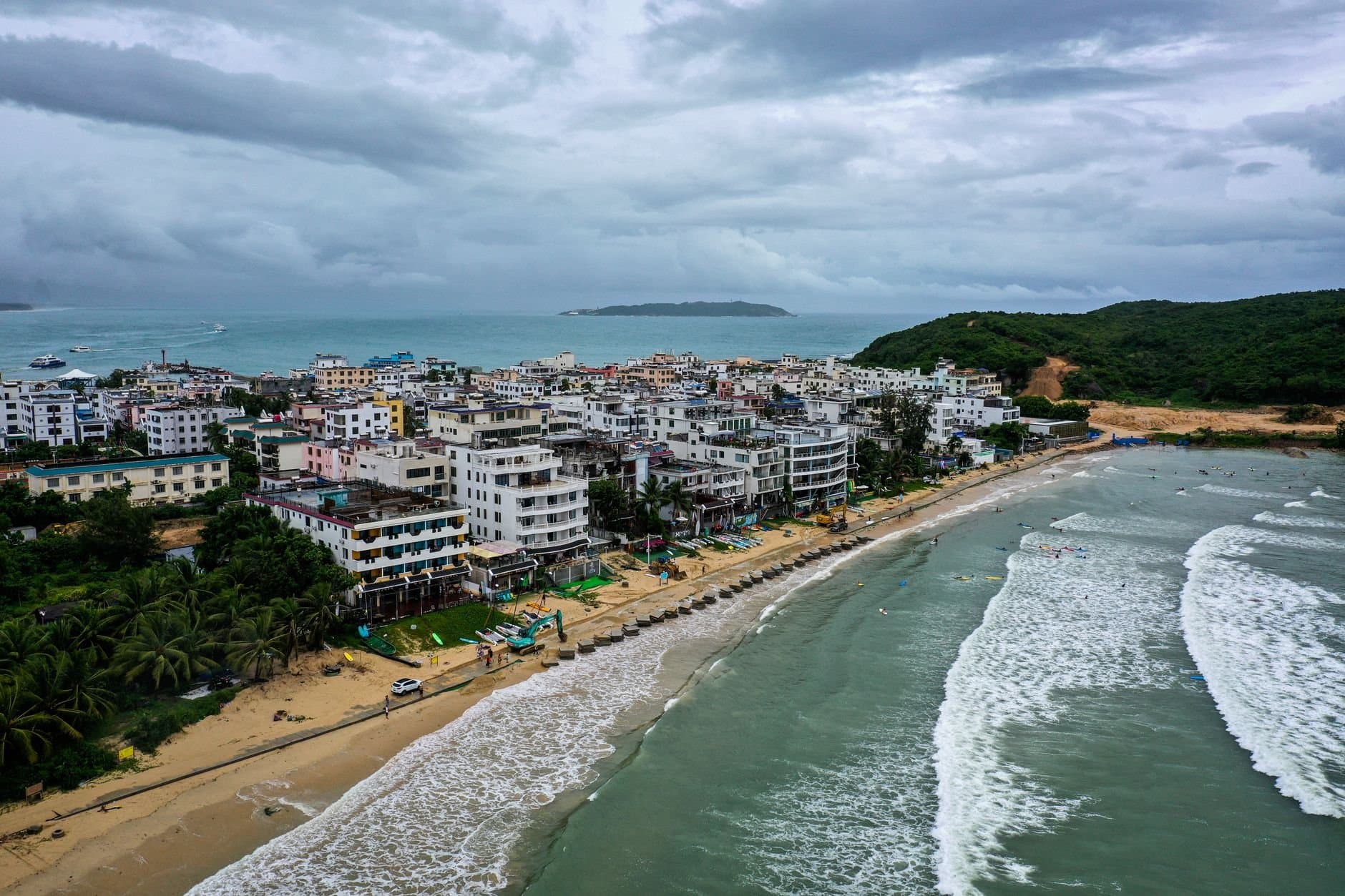 Drone captures vibrant Sanya coastline with beachfront buildings and lush greenery.