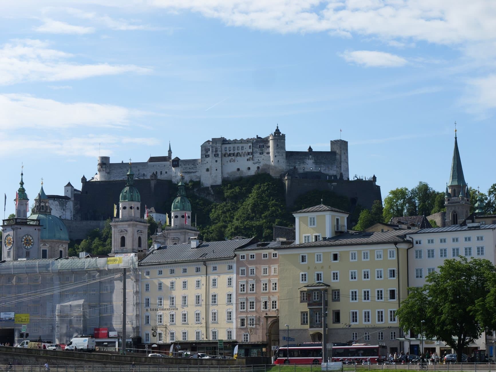 View of Hohensalzburg Fortress with historic Salzburg architecture and lush greenery on a sunny day.