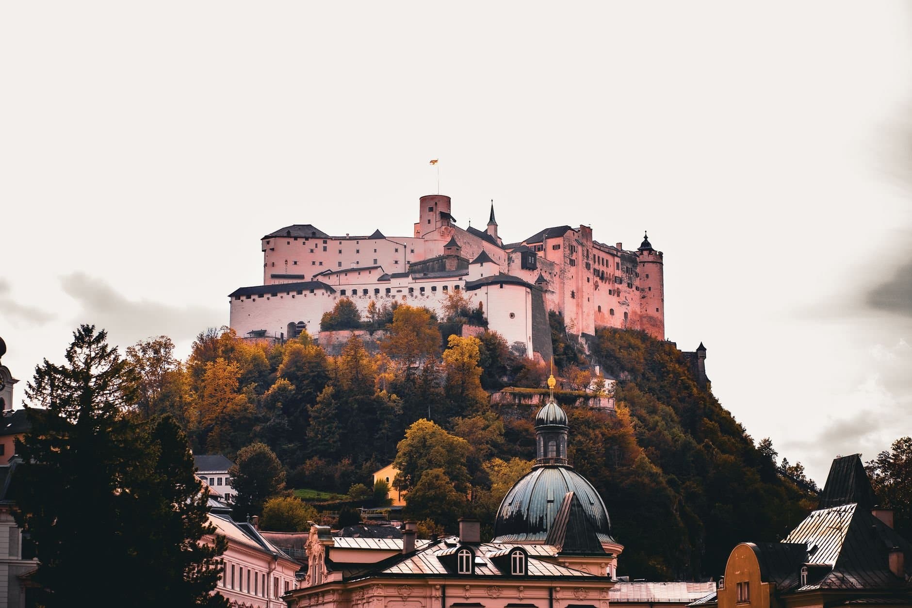 View of the Hohensalzburg Fortress atop a hill surrounded by vibrant autumn foliage in Salzburg, Austria.