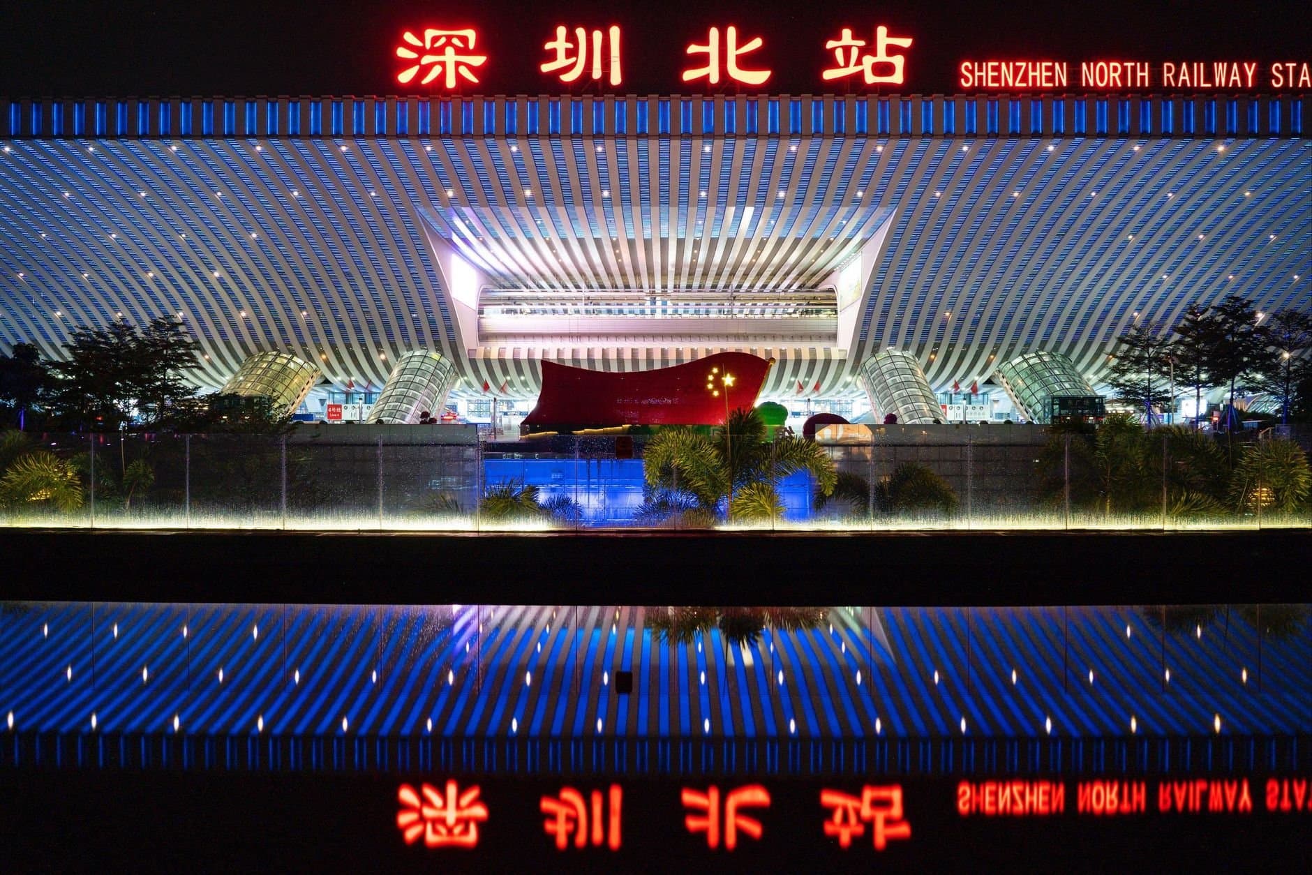 Shenzhen North Railway Station illuminated at night with vibrant lights and reflection.
